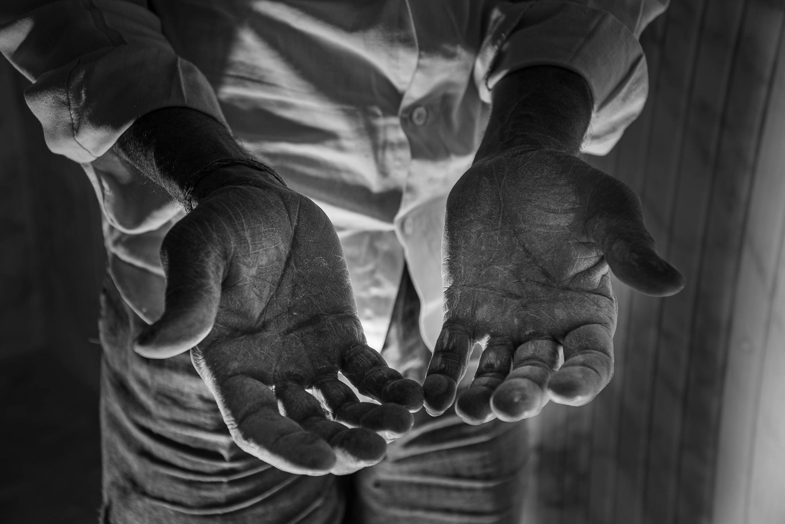 Black and white photo of a person wearing a shirt, with their hands extended toward the camera, palms facing up.