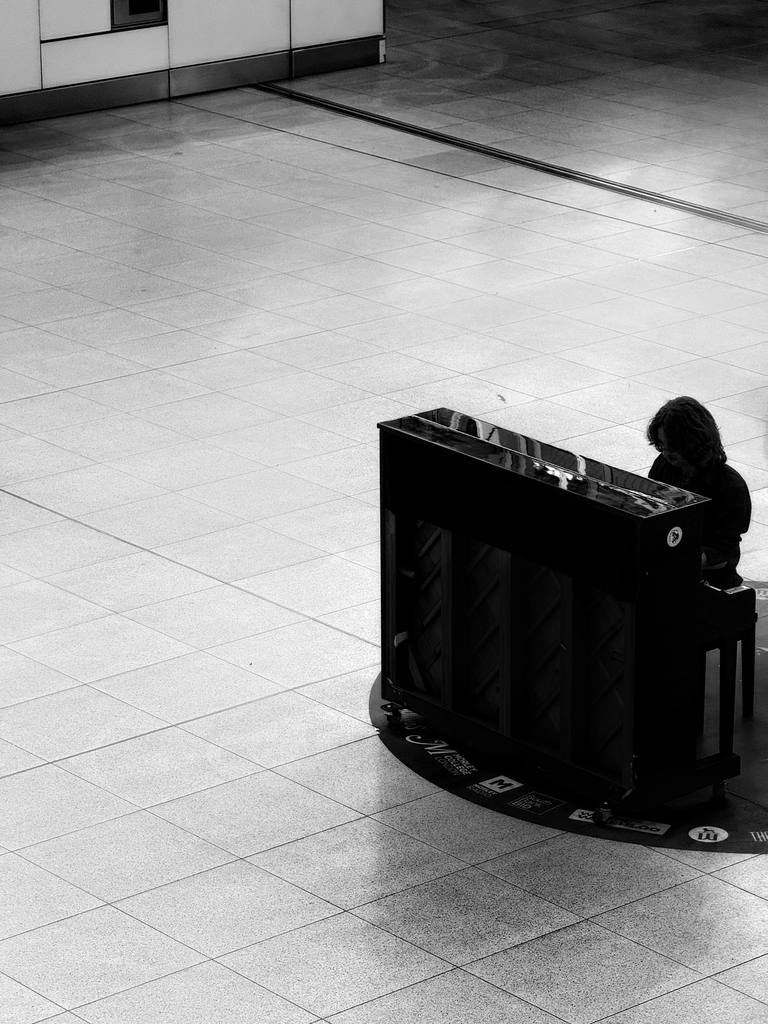A person playing a piano in an almost empty large indoor space with tiled floors.