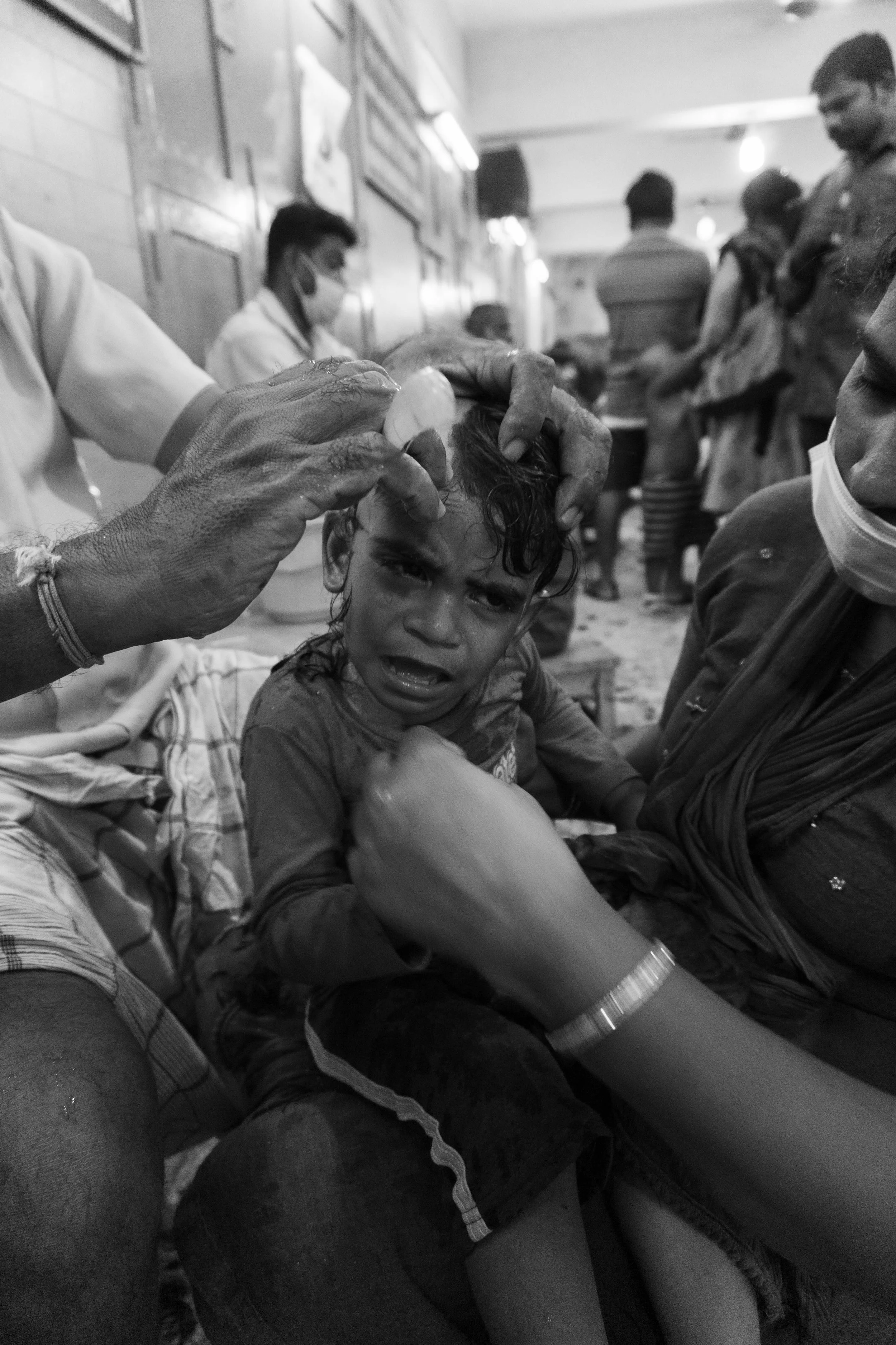 A young boy crying as a healthcare worker administers a vaccination to his forehead in a crowded indoor setting.