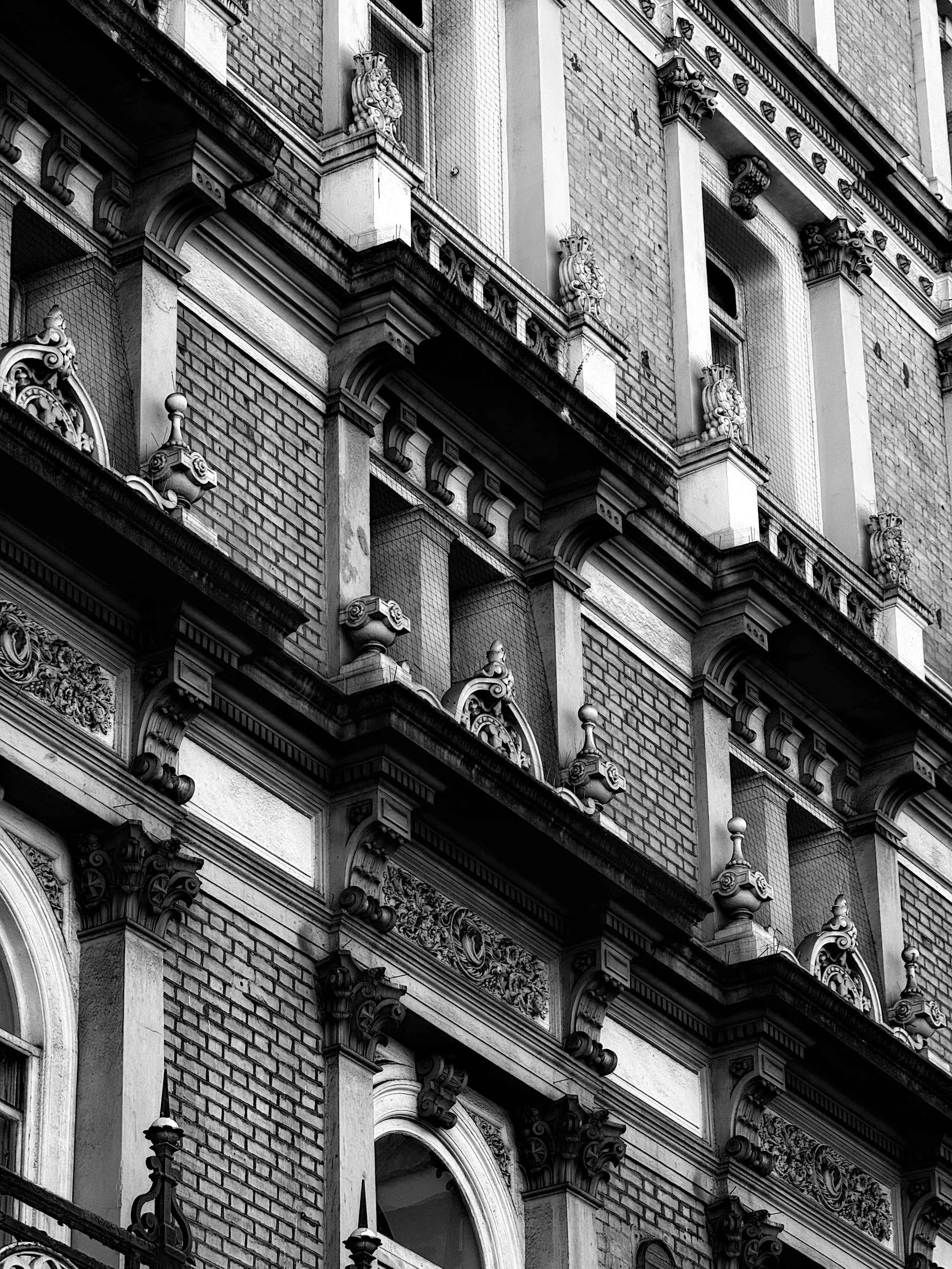 Black and white photo of a historic building's ornate façade with detailed architectural elements, including decorative moldings, columns, and balconies with intricate balustrades.