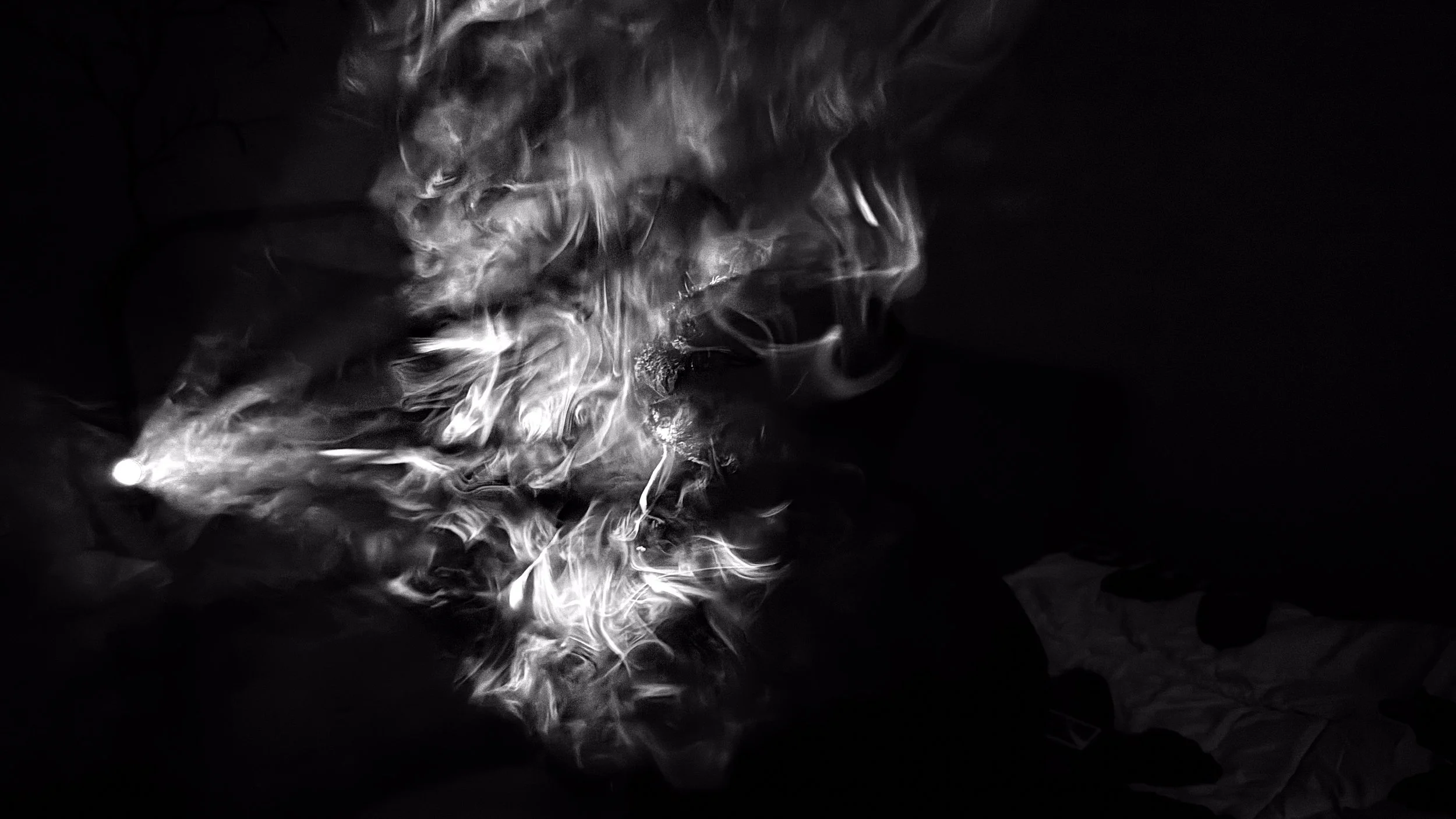 Black and white photo of swirling smoke or steam against a dark background, possibly coming from a lit object or source of heat.