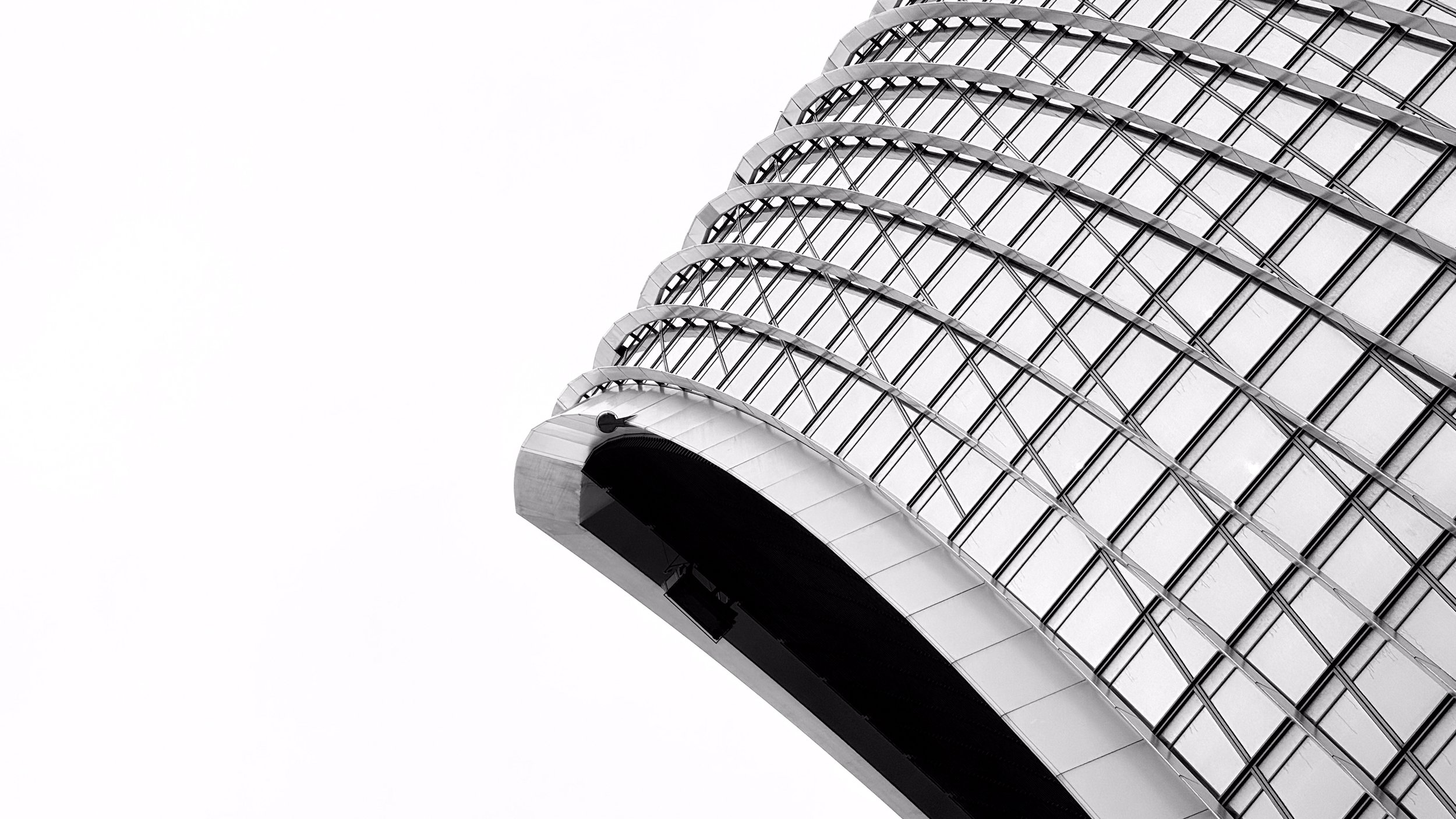 Close-up of a modern glass high-rise building with curved design, black accents, and metallic grid pattern against a white sky.