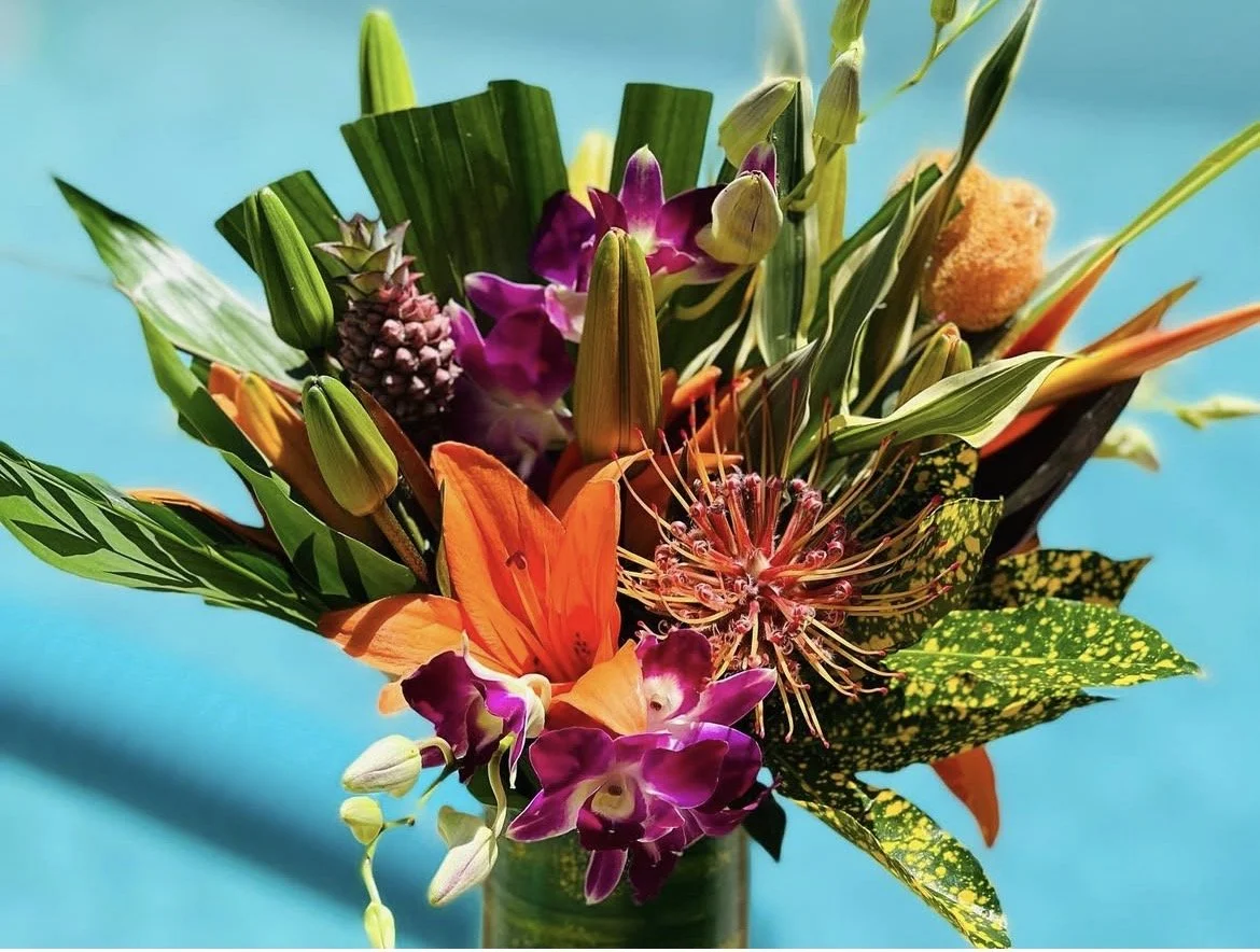 Colorful tropical flower bouquet with orange, purple, and pink flowers over a blue background.