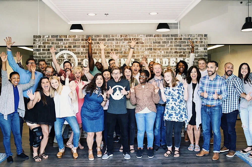 Group of diverse people celebrating indoors, smiling with raised hands.
