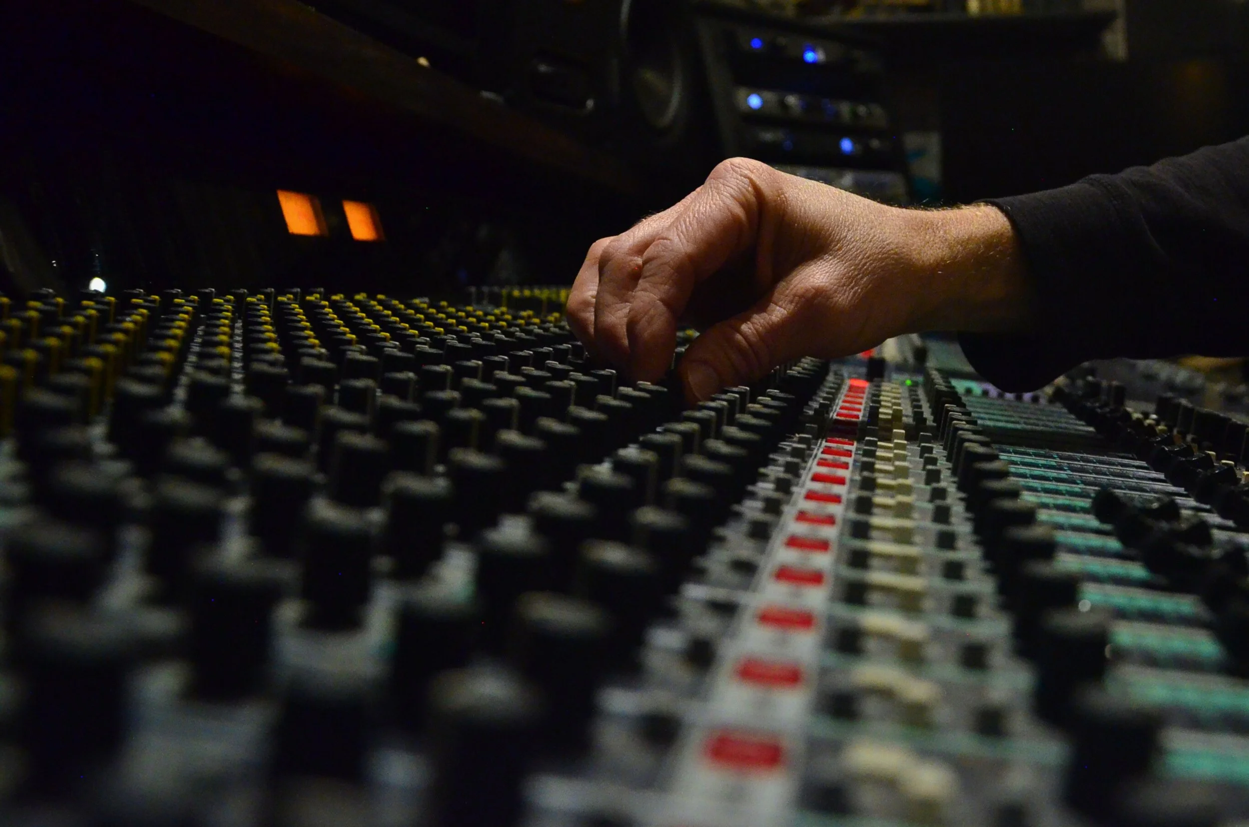 Close-up of a person adjusting sound mixing console controls in a dark studio.