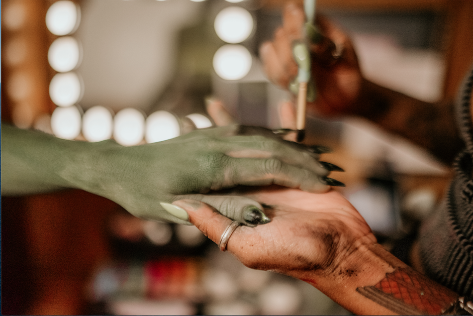 A person with green skin getting their nails painted by another individual with painted and unnatural colored nails.