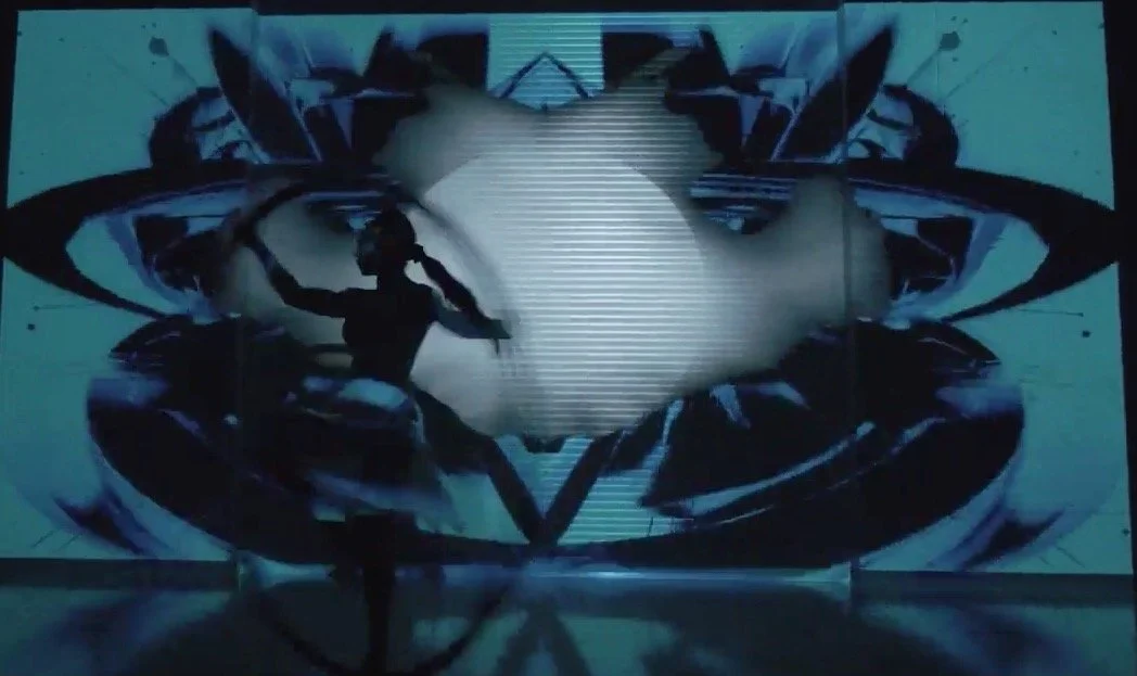 A silhouette of a person standing in front of a large digital screen with abstract artwork and patterns.