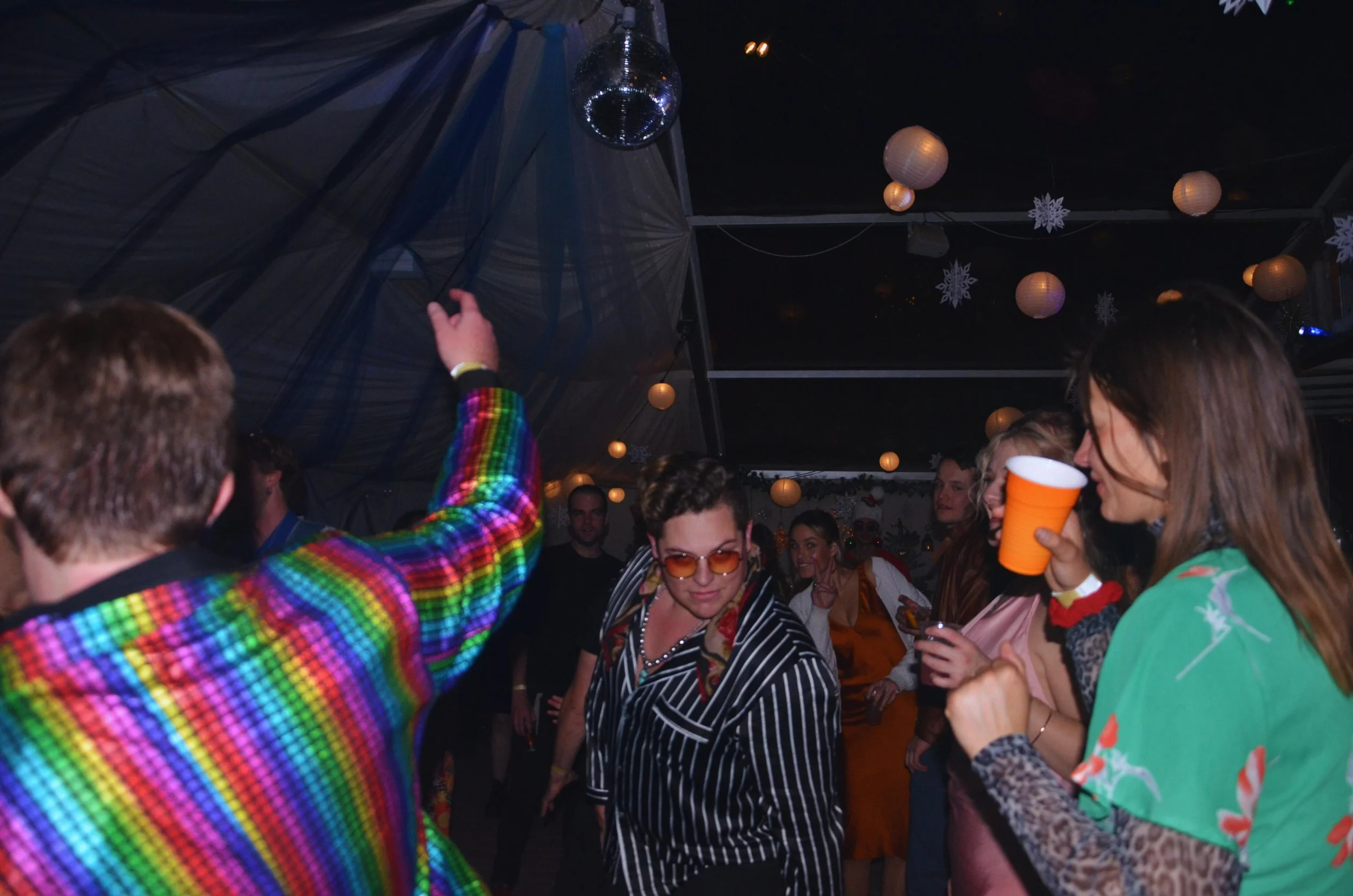 People dancing and socializing at a party with festive decorations, including paper lanterns and snowflakes, under a disco ball.