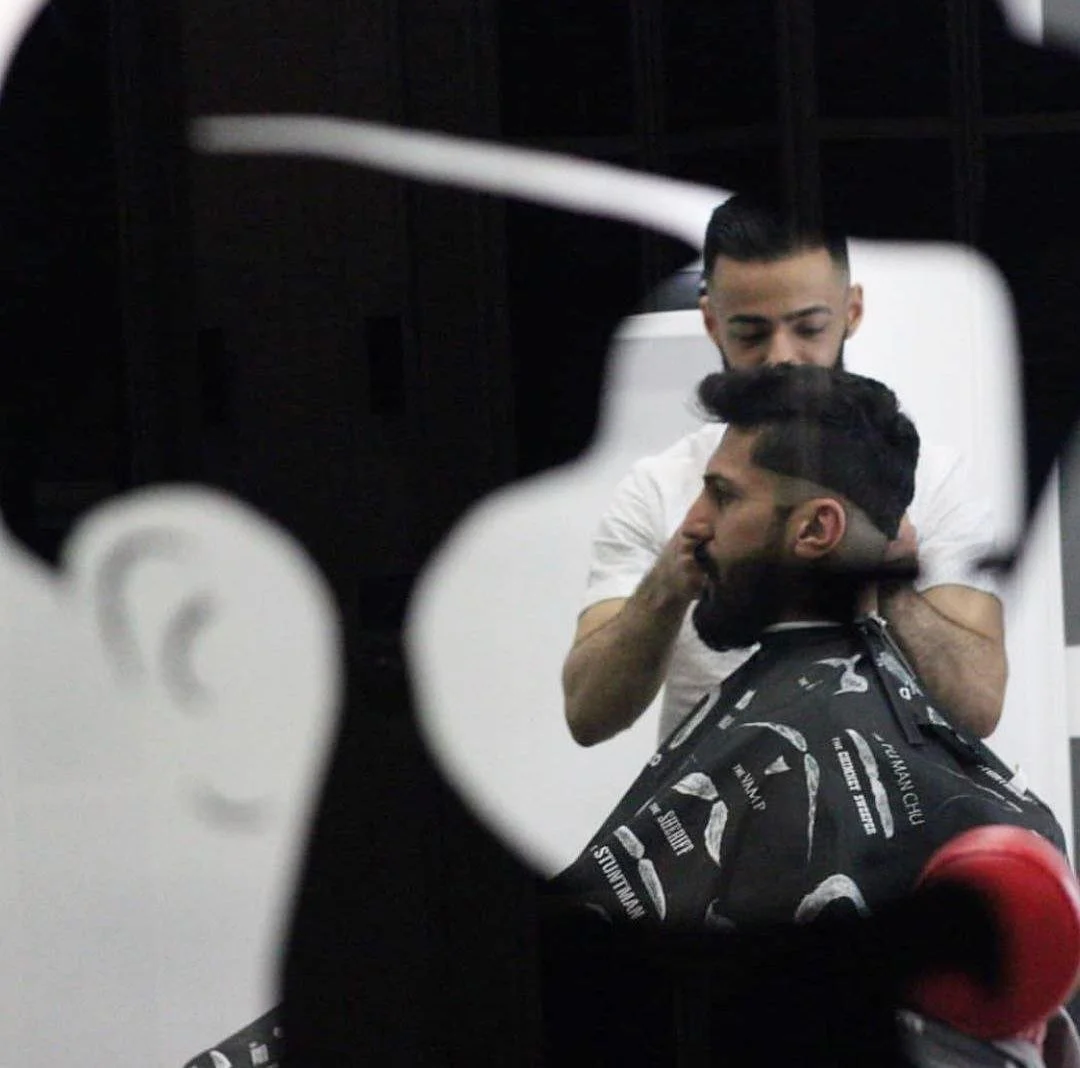 A man having his hair cut at a barber shop, seen through a decorative mirror.