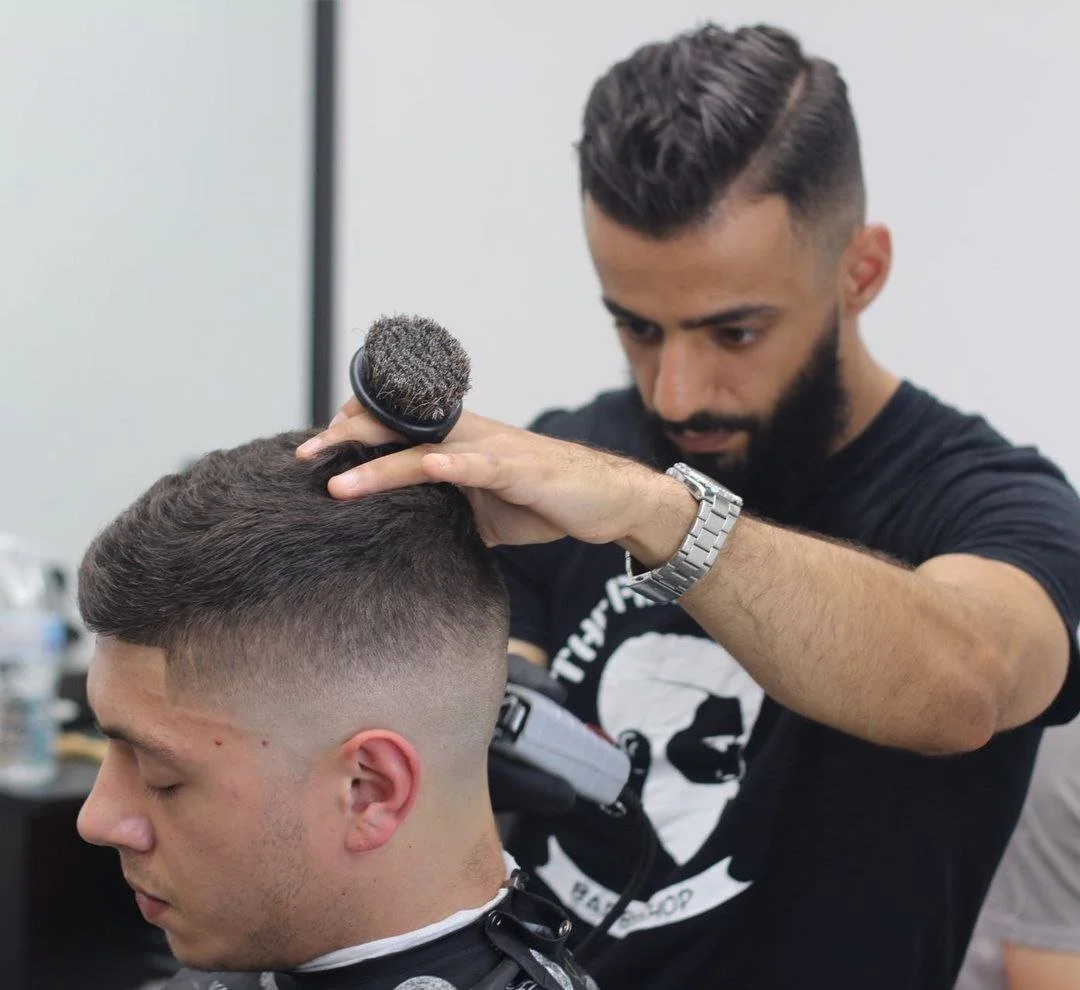 Barber using a clipper to trim a man's hair in a salon.