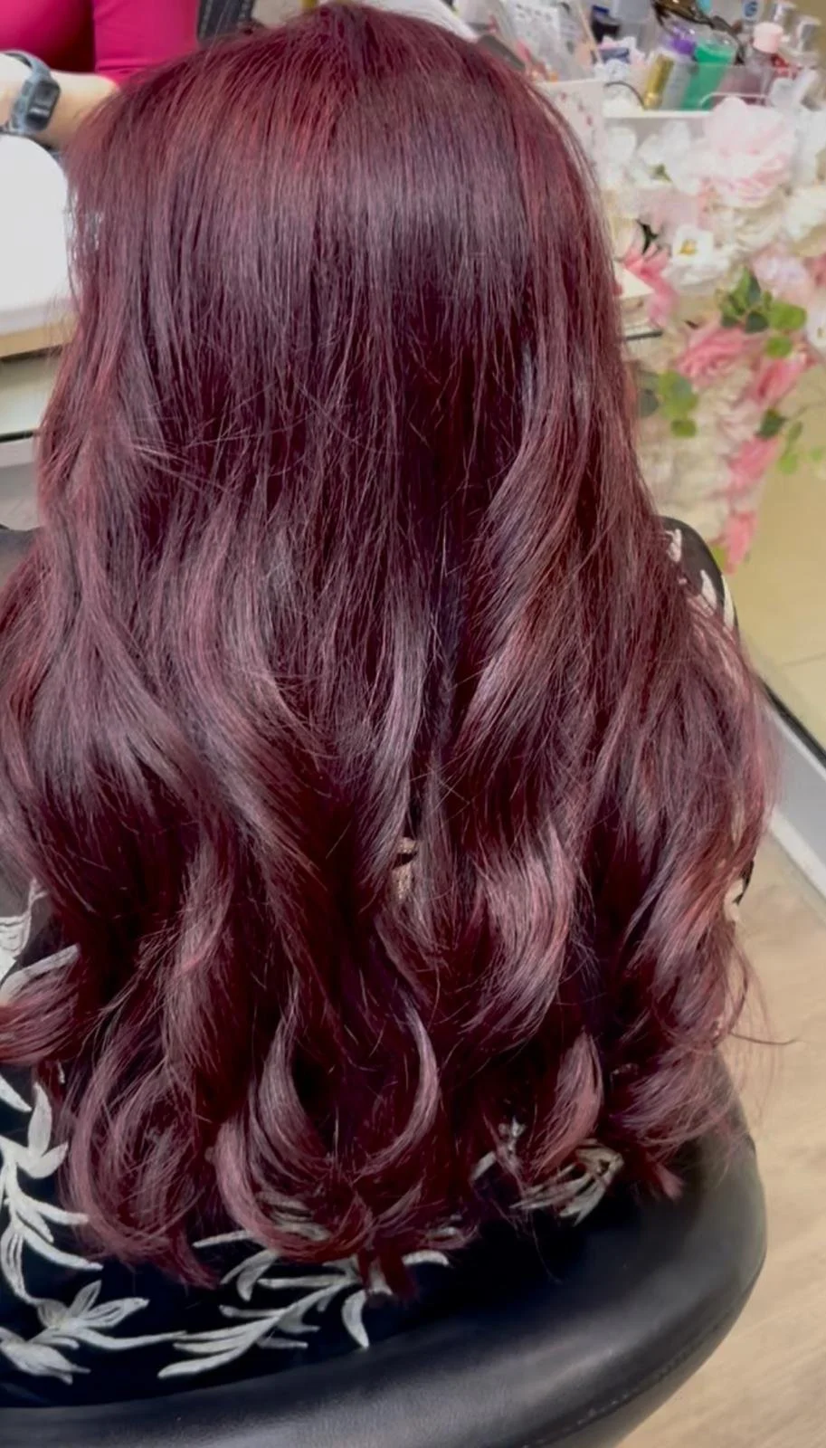 A person with long, wavy burgundy-colored hair sitting in a salon chair.