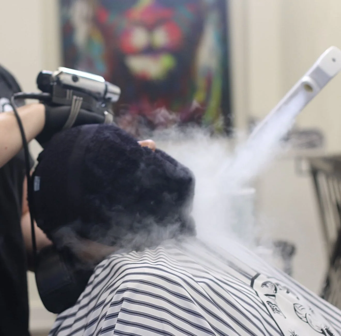 A person receiving a barber shave at a barbershop, with vapor or steam rising from the face.