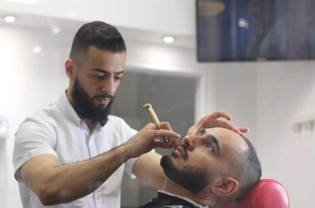 Barber applying makeup or cosmetics to a client in a barber shop.