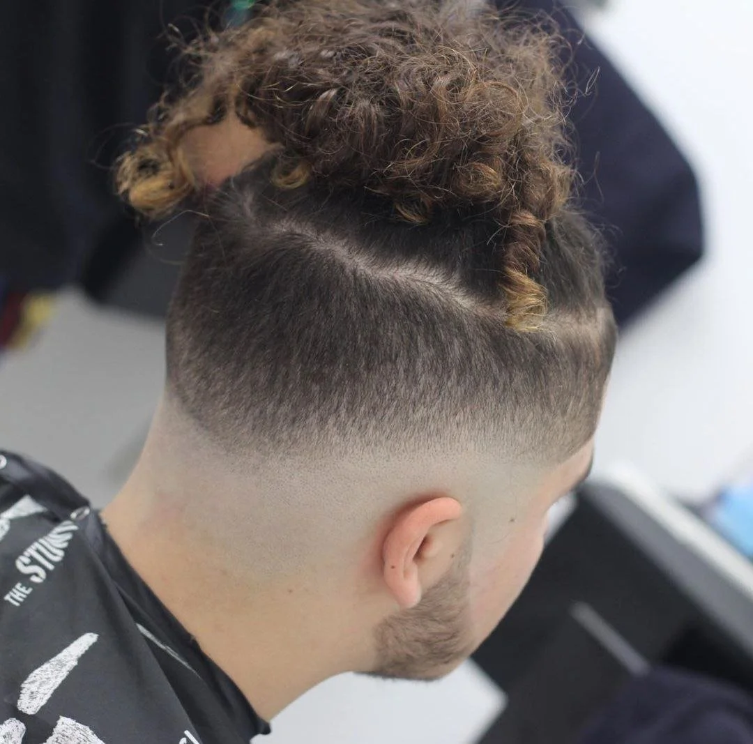 Close-up of a man's hairstyle showing a fade cut with curly hair on top.
