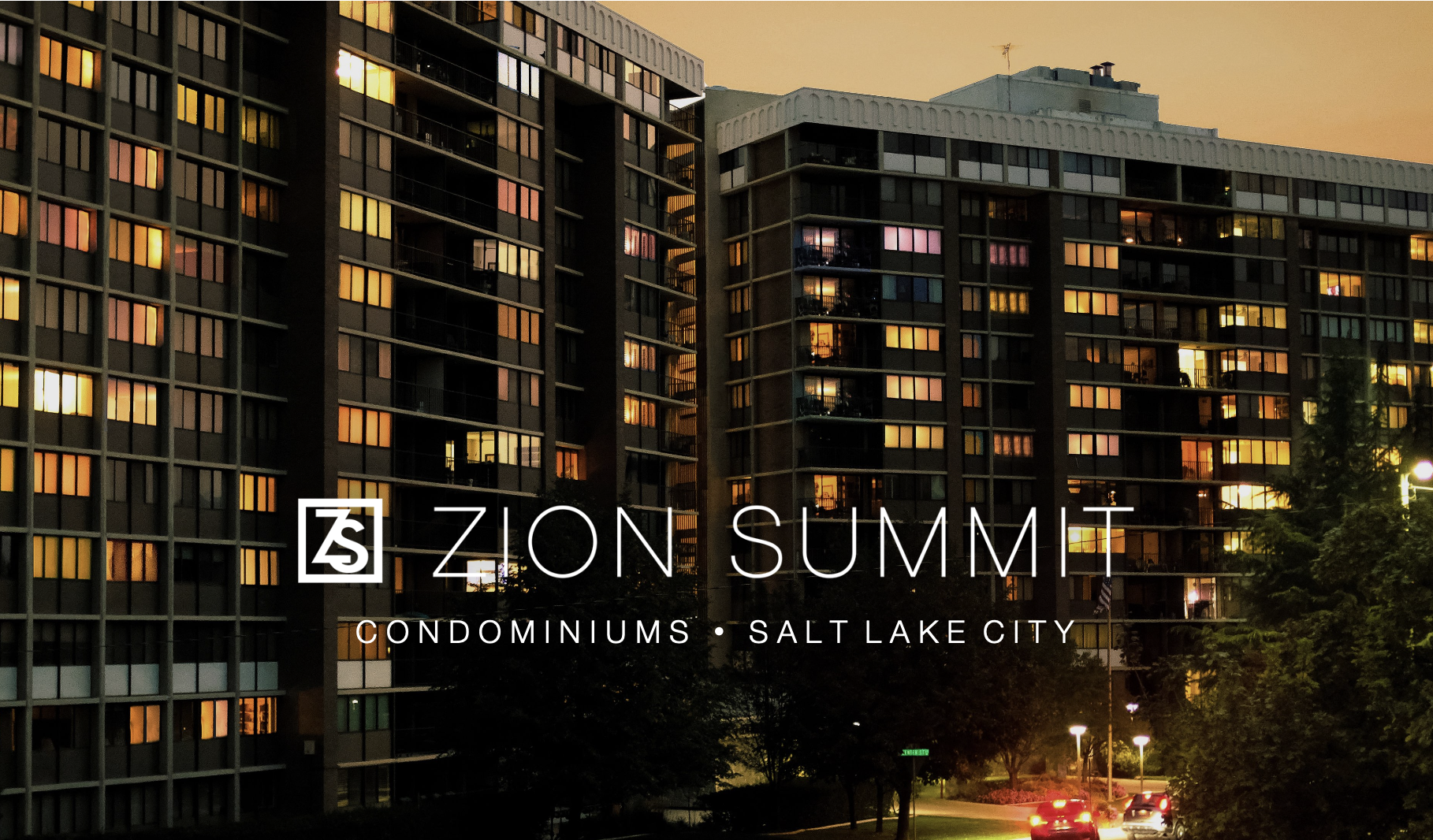 Sunset over high-rise condominiums in Salt Lake City with illuminated windows and a street with cars and trees in the foreground.