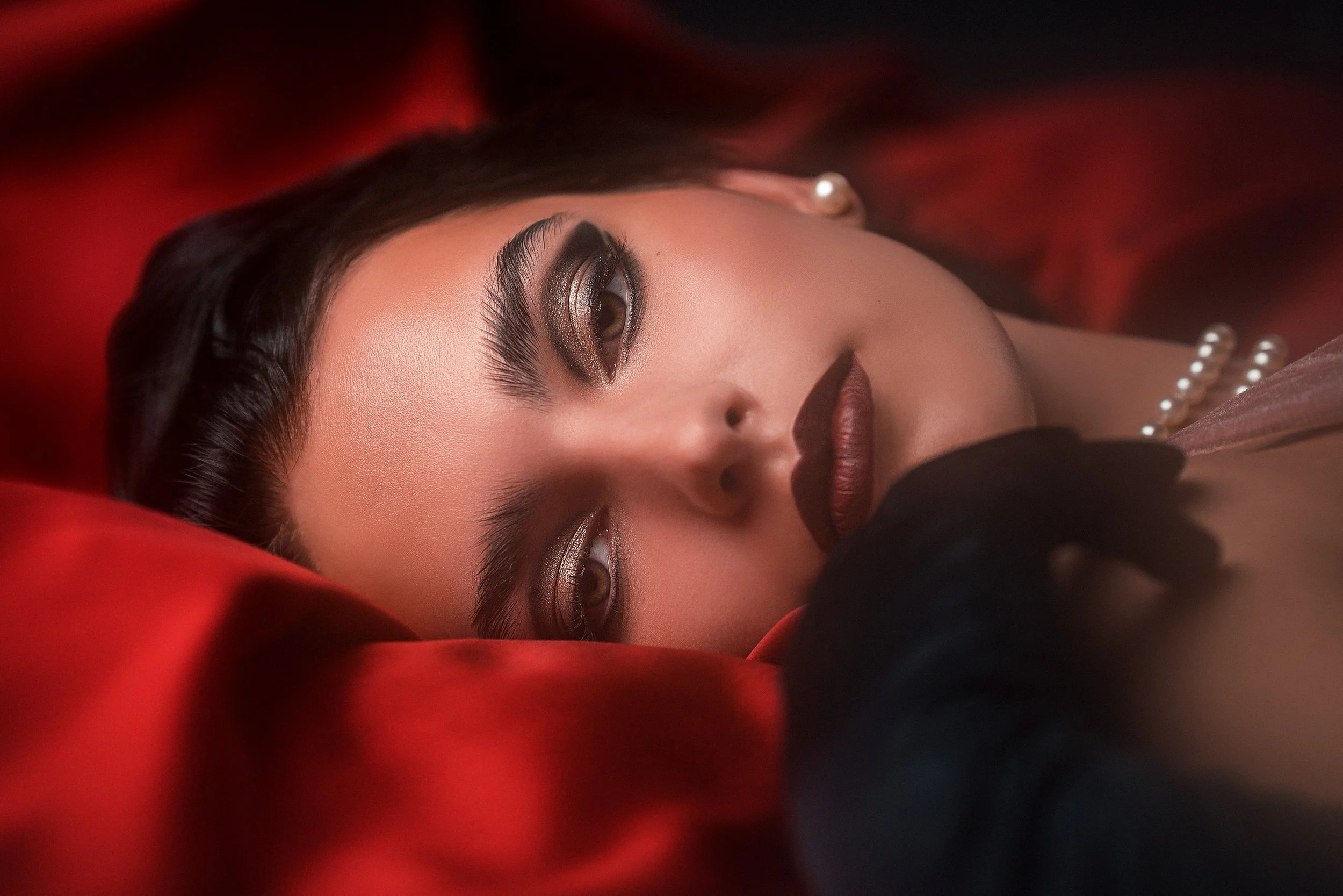 Oona Antila makaa punaisen silkkikankaan päällä film noir -tyylisessä femme fatale -henkisessä headshot-muotokuvassa. Meikki ja hiukset: Nina Vuori. Muotokuvaus Helsinki – hyvän mielen valokuvaaja Sami Turunen.
