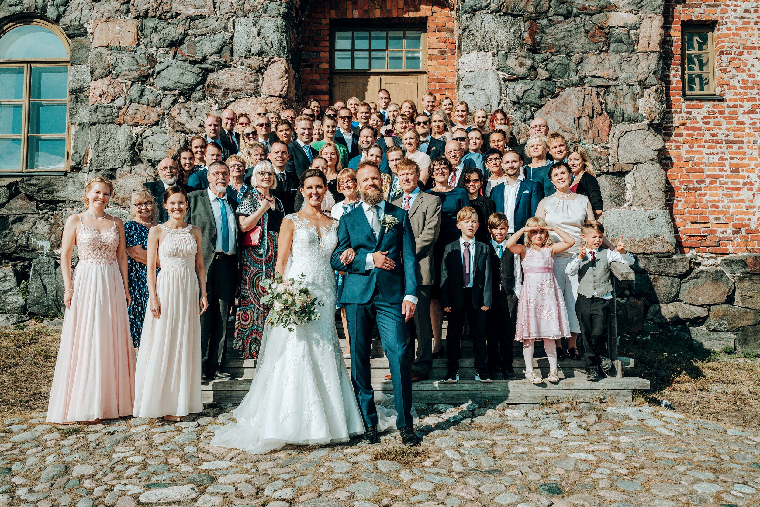 Hääpari ja juhlaväki Pirunkirkon edustalla Suomenlinnassa. Hääkuvaus Helsinki - Hyvän mielen hääkuvaaja Sami Turunen.