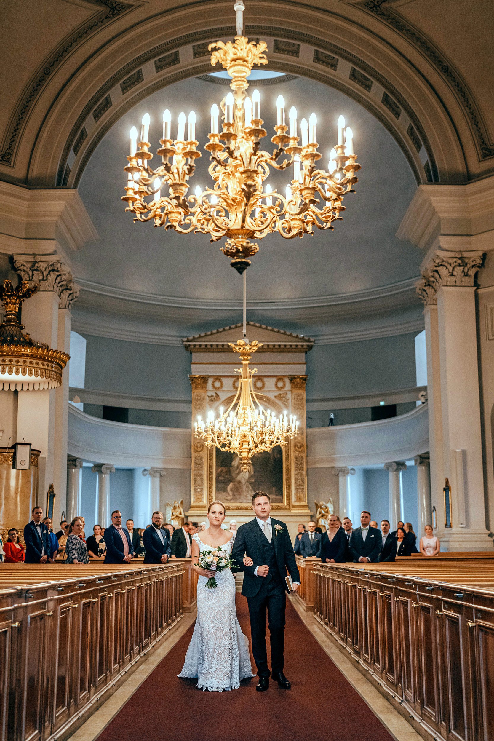 Vastavihitty hääpari kävelee Helsingin tuomiokirkon majesteettisten holvikaarien alla. Hääkuvaus Helsinki – hyvän mielen hääkuvaaja Sami Turunen.