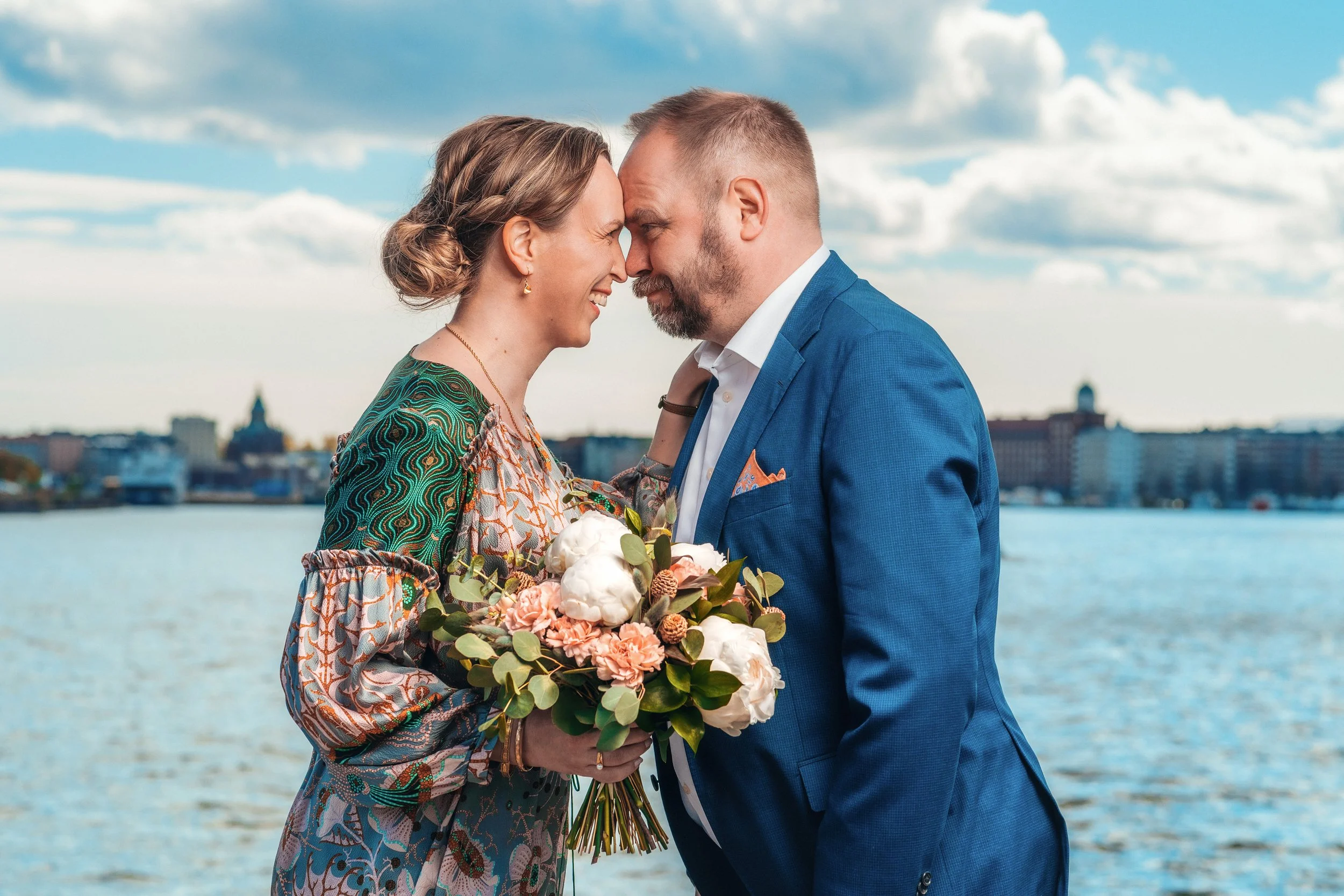 Hääpari humoristisessa potretissa Kalasatamassa. Taustalla piirtyy merimaisema ja Helsingin kantakaupungin siluetti. Hääkuvaus Helsinki - Hyvän mielen hääkuvaaja Sami Turunen.