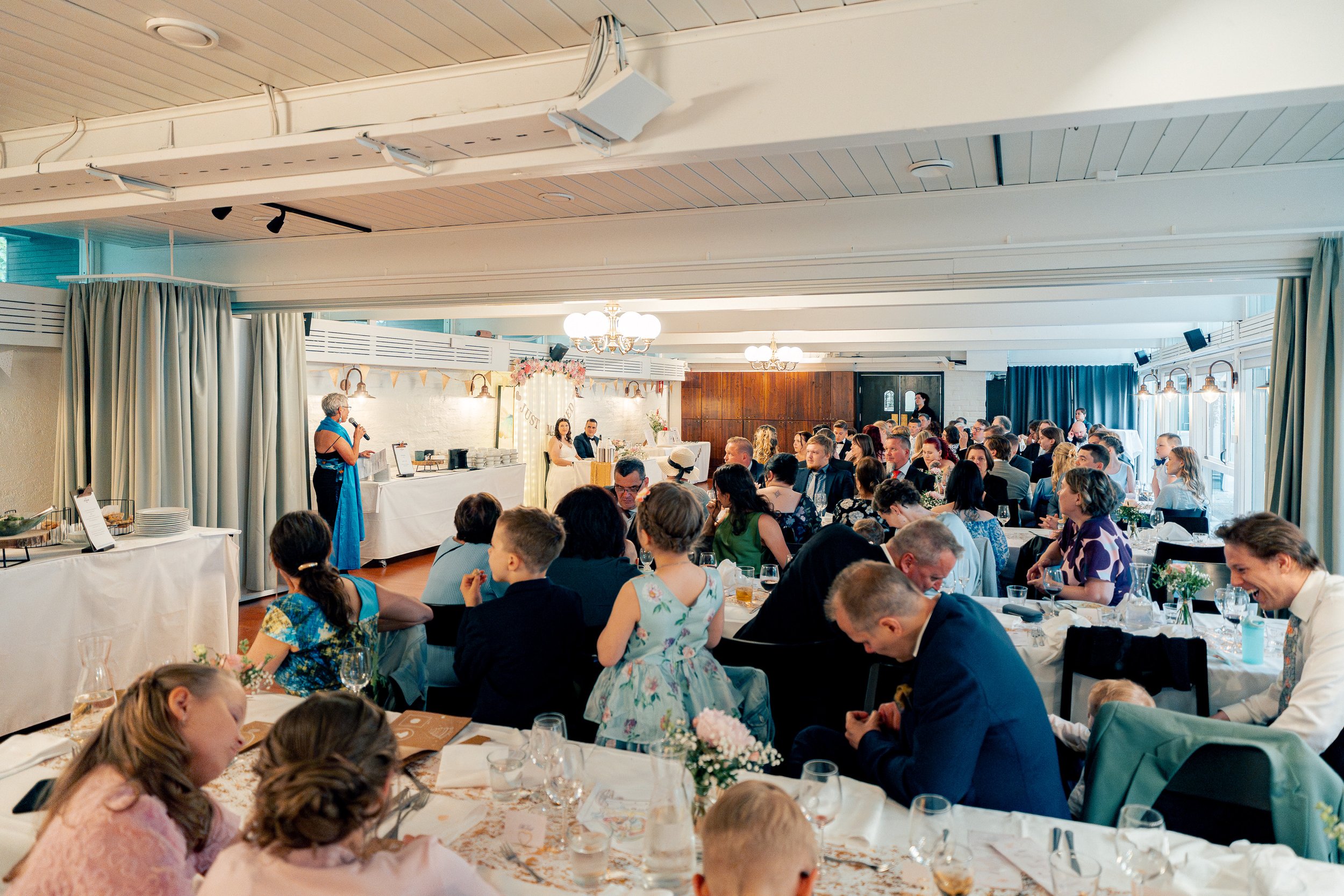 Sulhasen äiti naurattaa puheellaan hääparia ja juhlaväkeä Mestaritallissa Helsingissä. Hääkuvaus Helsinki - Hyvän mielen hääkuvaaja Sami Turunen.