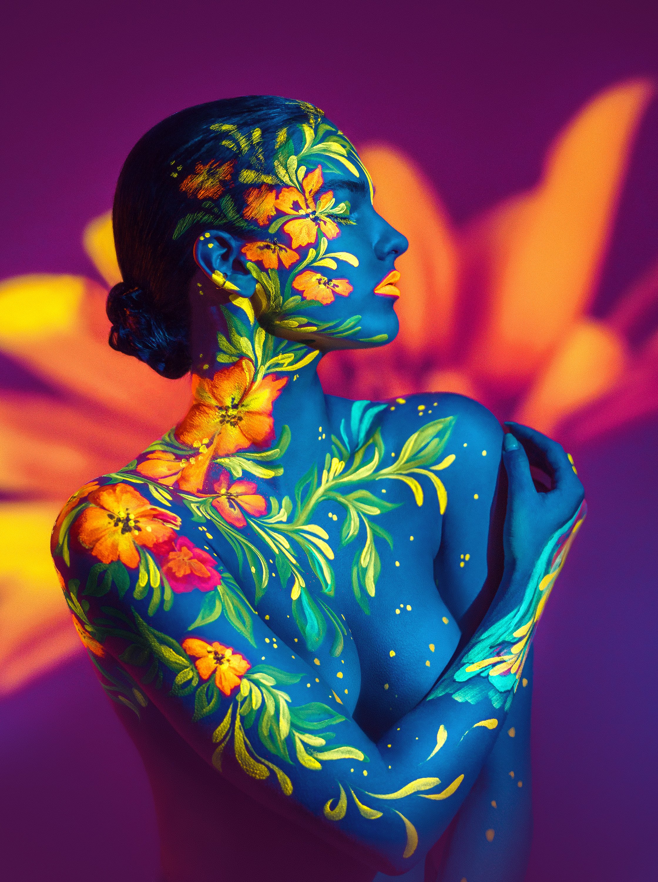 Oona Antila taiteellisessa bodypainting-kuvassa, jossa UV-valot korostavat maalattujen värien loistetta. Taustalla videotykillä heijastettu kukka. Bodypainting-taiteilija: Riina Laine. Luova muotokuvaus Helsinki – hyvän mielen valokuvaaja Sami Turune