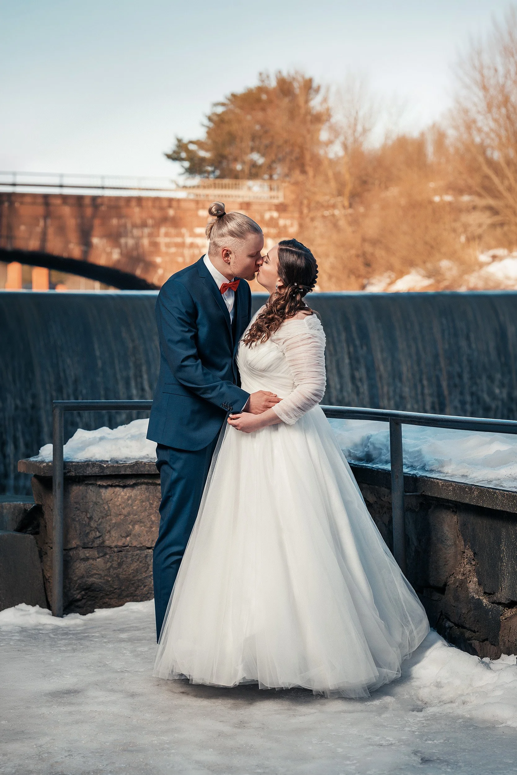 Hääpari suutelee talvimaisemissa kuohuvan Vanhankaupunginkosken edessä Helsingissä. Hääkuvaus Helsinki - Hyvän mielen hääkuvaaja Sami Turunen.