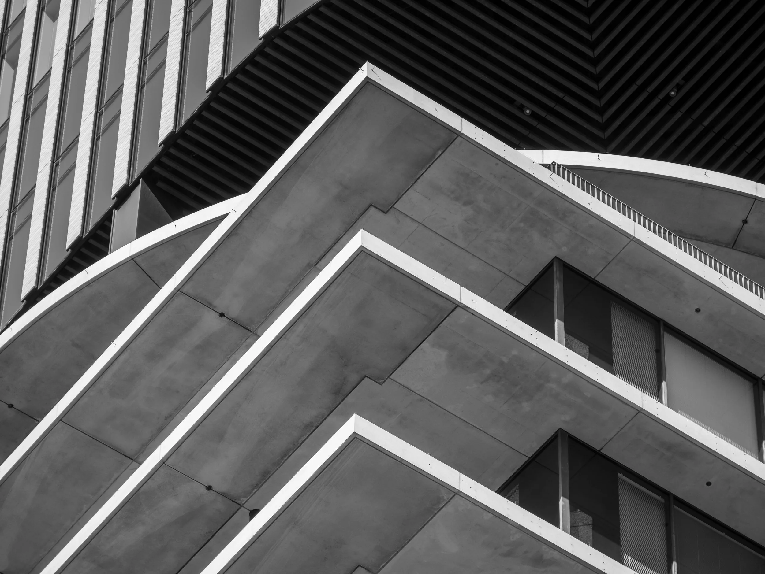 Close-up view of a modern building's exterior, showcasing angular concrete balconies and glass windows, with a black and white filter highlighting architectural details.