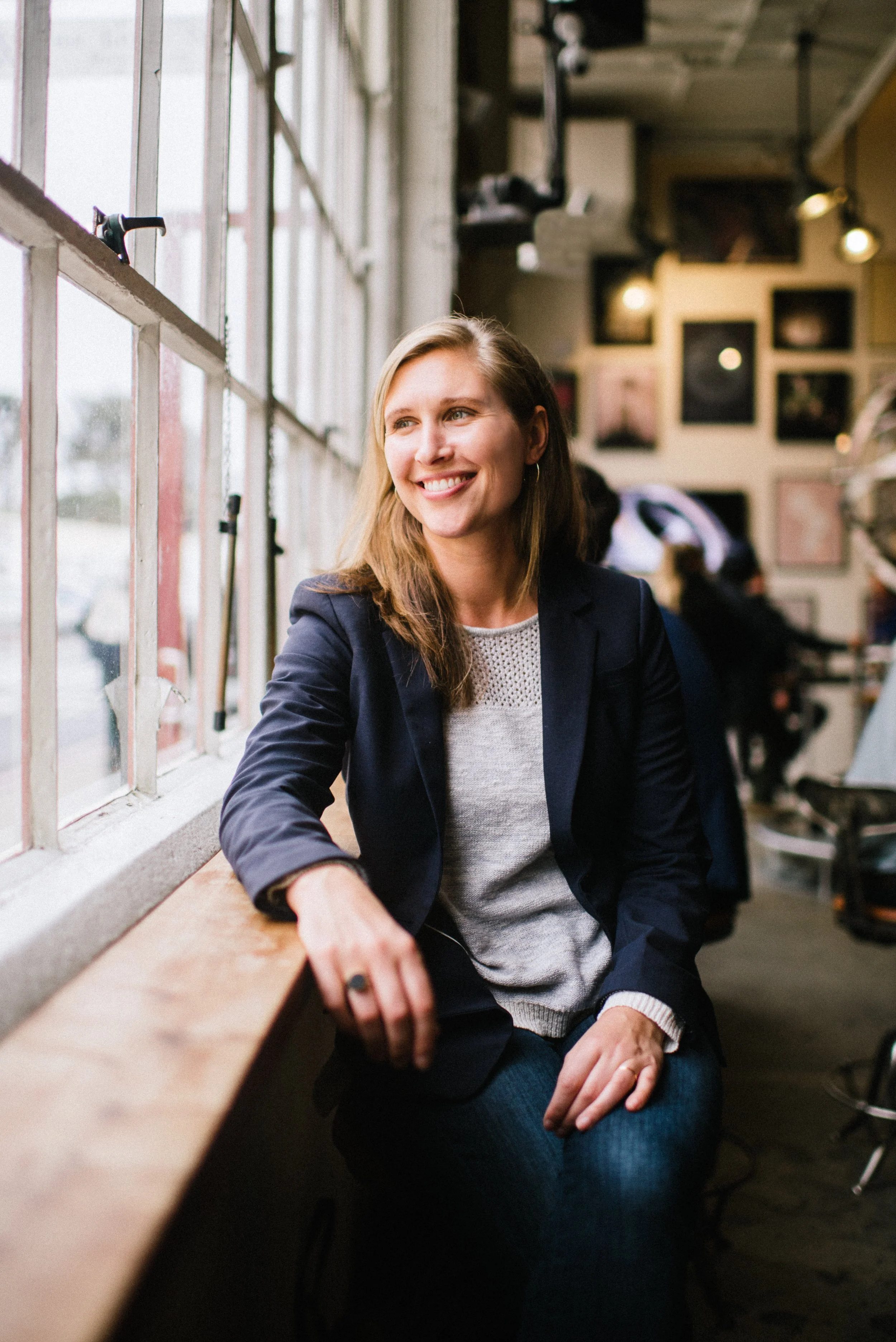 A woman smiling while sitting near a window in a café or restaurant.