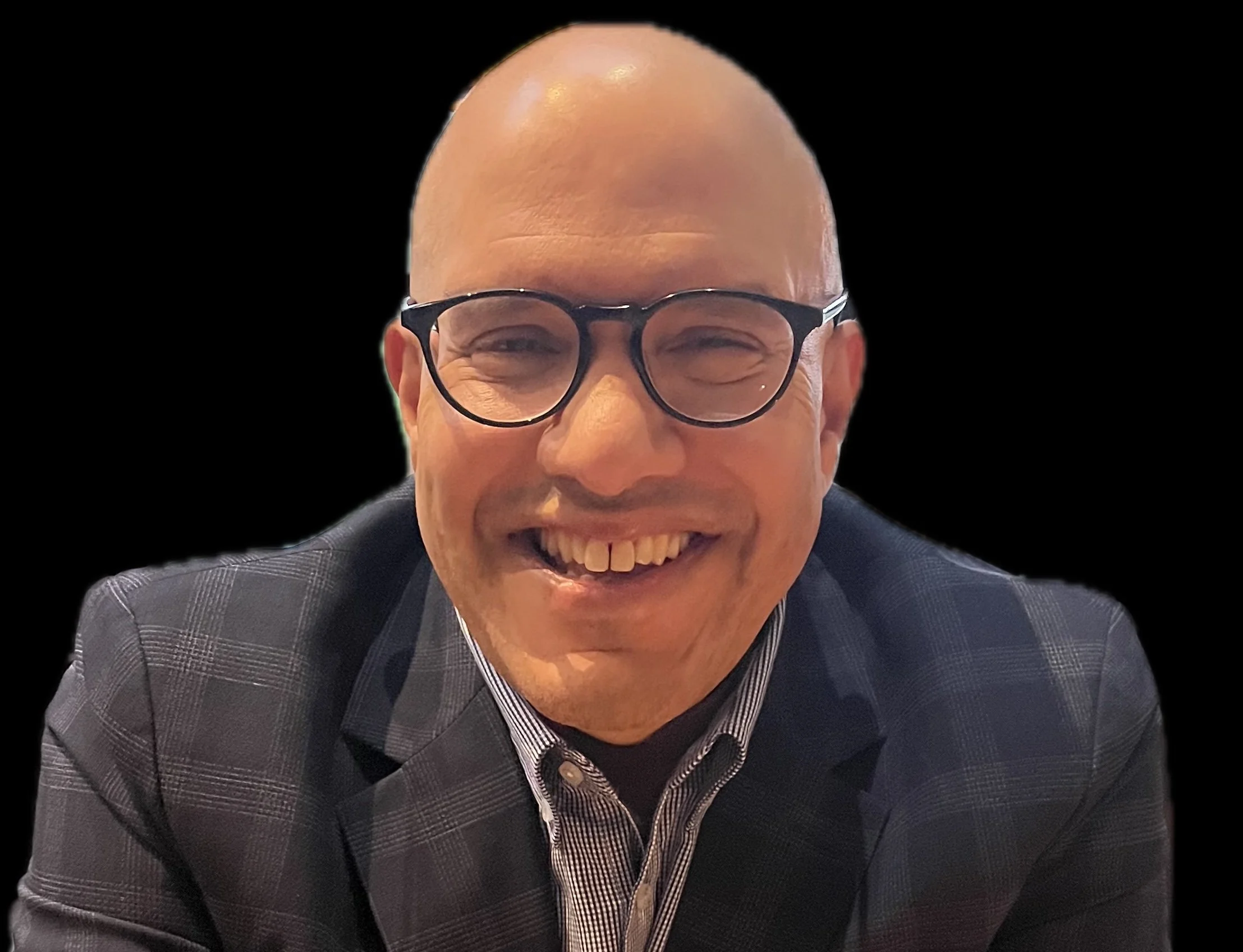 A smiling man with glasses, wearing a checked blazer and striped shirt, posing against a black background.