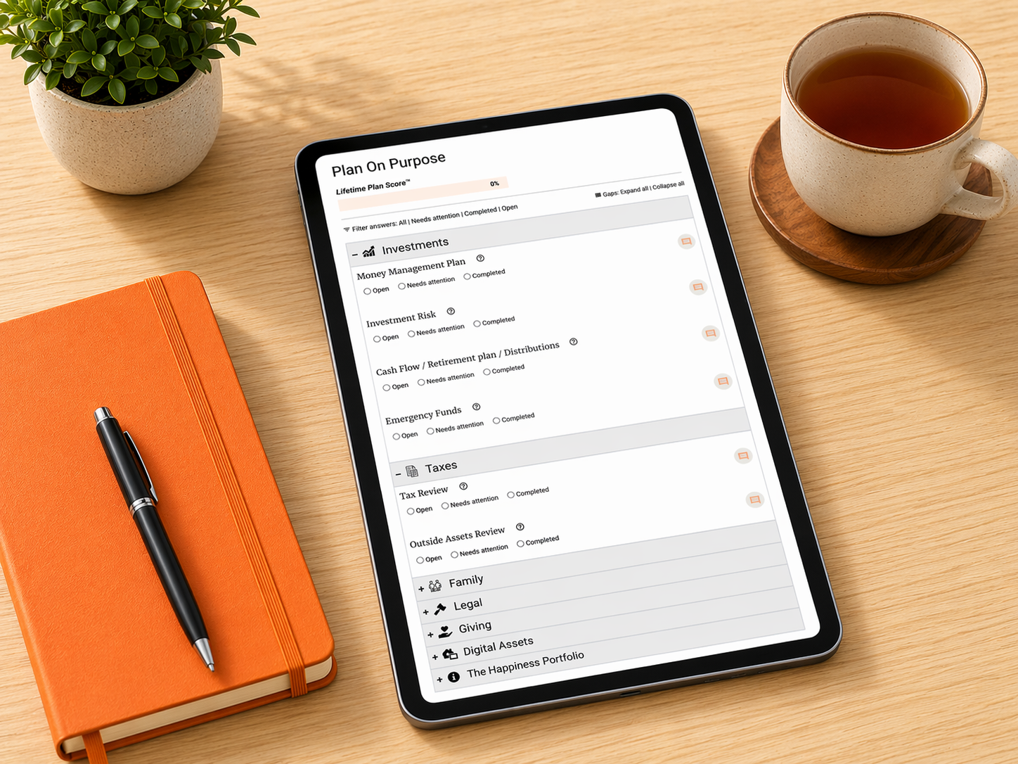 A tablet displaying a financial planning app on a wooden desk, next to an orange notebook with a black pen, a cup of tea on a wooden coaster, and a potted plant.