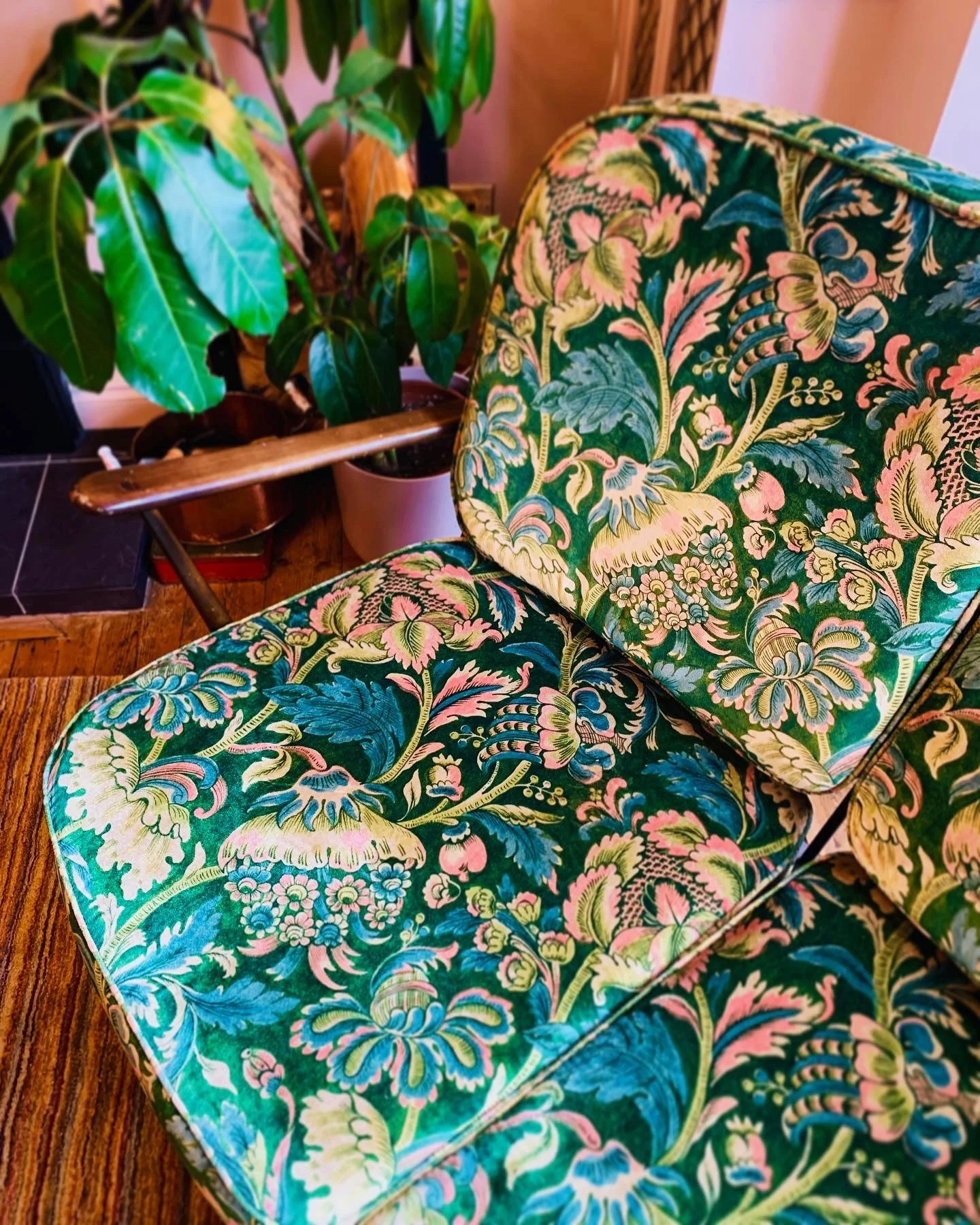 Close-up of a floral-patterned upholstered chair with green, pink, and blue designs, next to potted plants on a wooden surface.