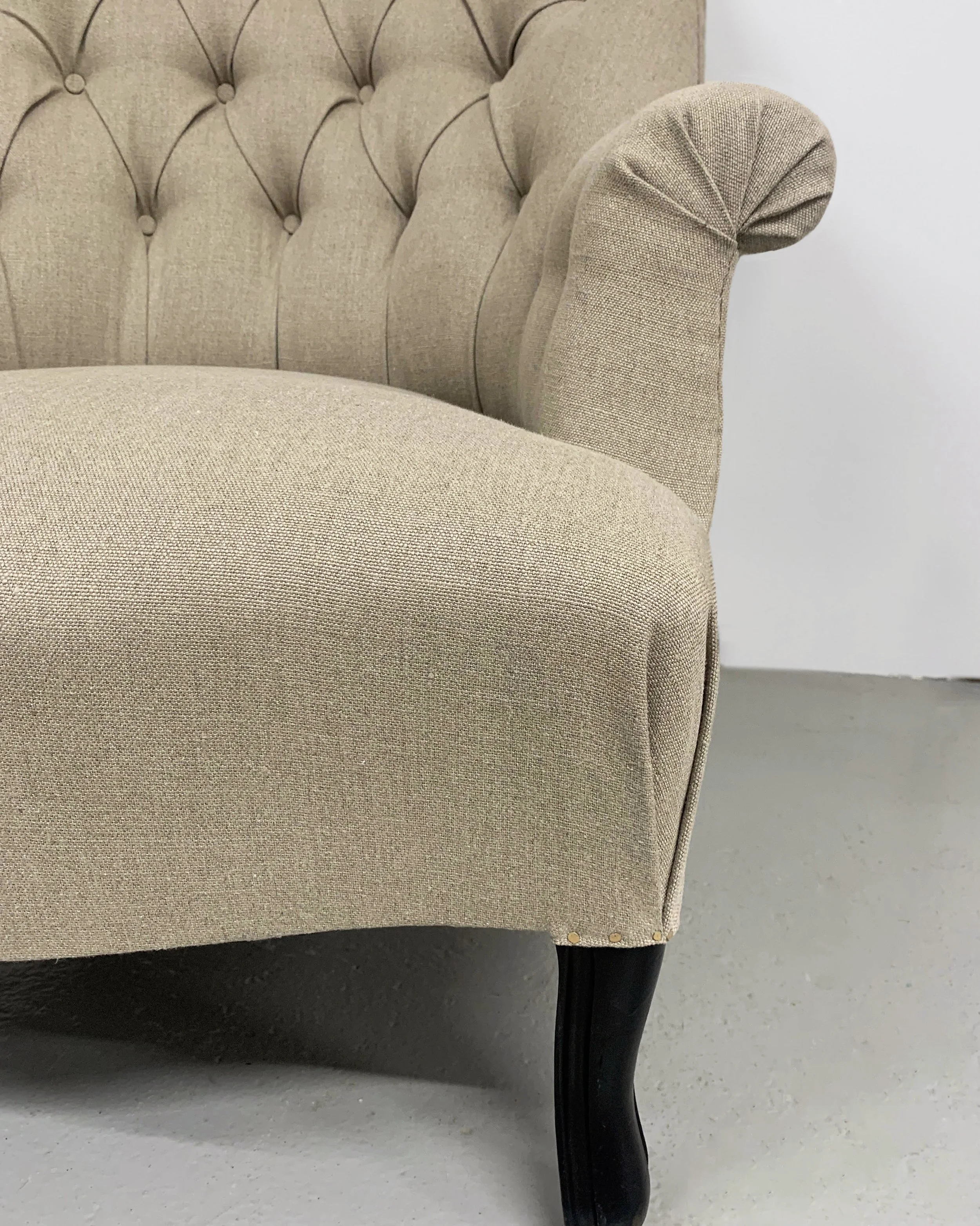 Close-up of a beige upholstered armchair with tufted back, rolled armrest, and wooden cabriole legs.
