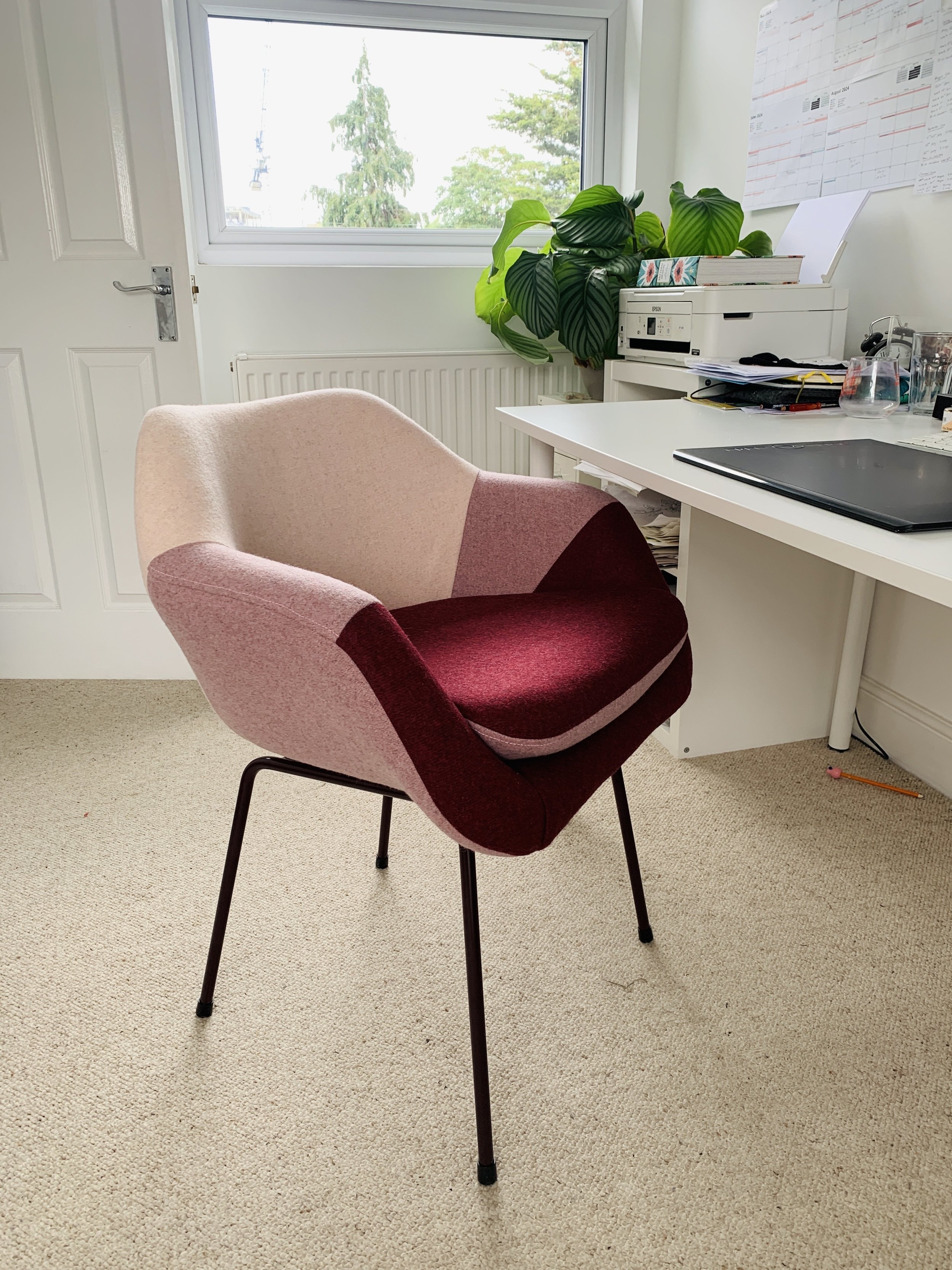 A colorful chair in a home office space with a white desk, a window, and a large green plant.