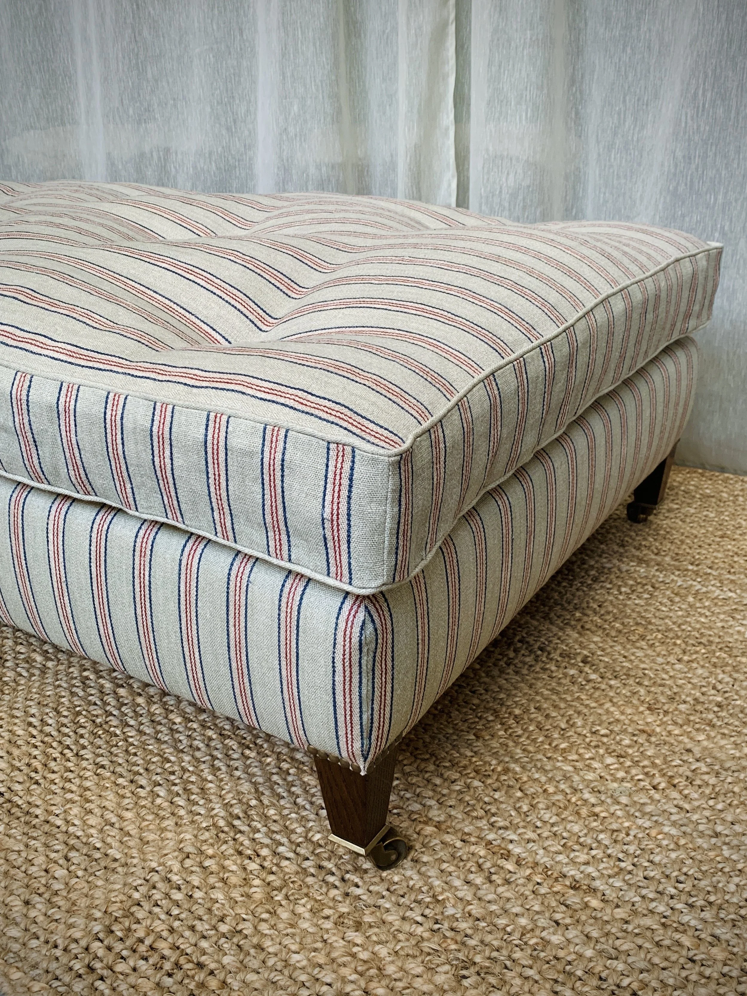 A striped upholstered chaise lounge with wooden legs and small casters on a textured beige carpet.