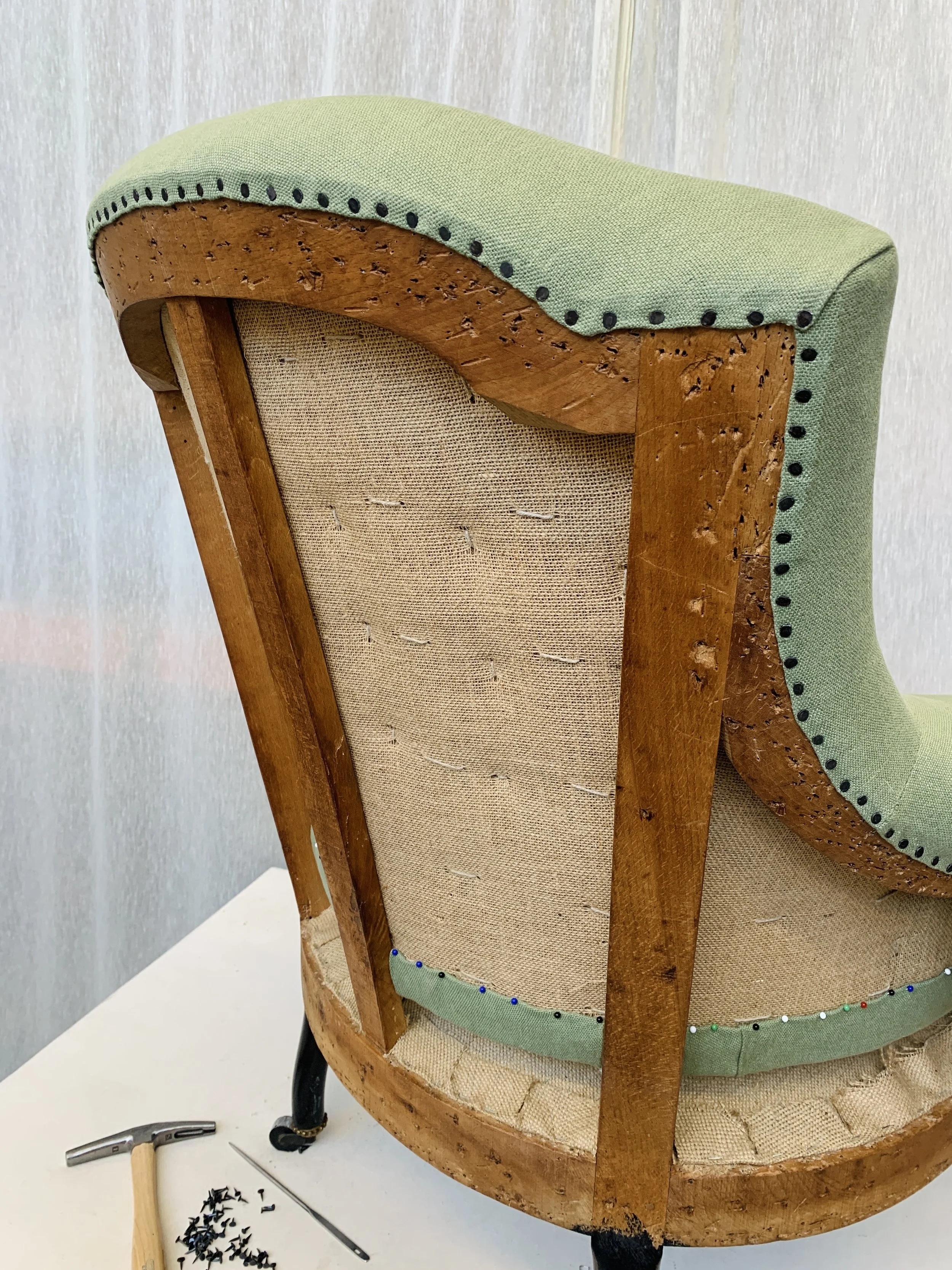 Close-up of the back of an antique wooden chair with upholstery, showing the wood frame, fabric, and nail details.
