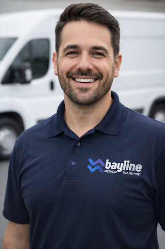 A smiling man wearing a navy blue polo shirt with the 'Bayline Medical Transport' logo, standing outdoors with a white van in the background.