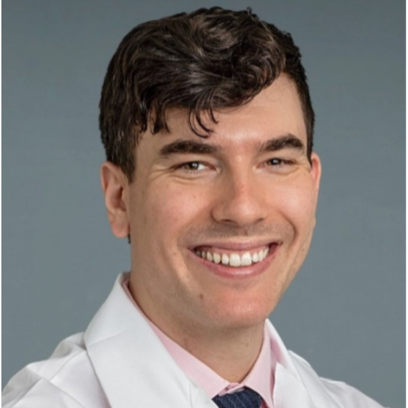 A smiling man wearing a white lab coat and a pink shirt with a dark tie, against a plain gray background.