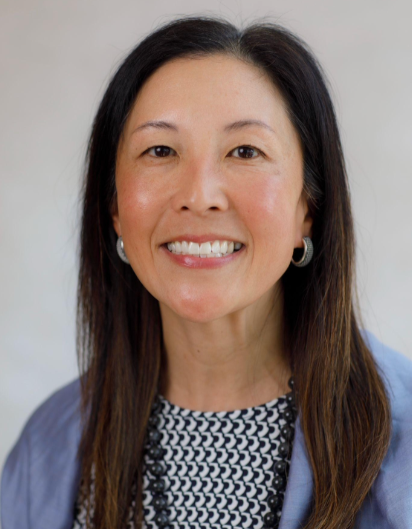 A woman with long dark hair wearing a light blue blazer and patterned top, smiling at the camera.