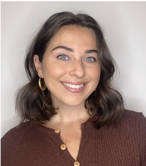 A woman with shoulder-length brown hair, blue eyes, and a bright smile wearing a maroon sweater and gold hoop earrings.