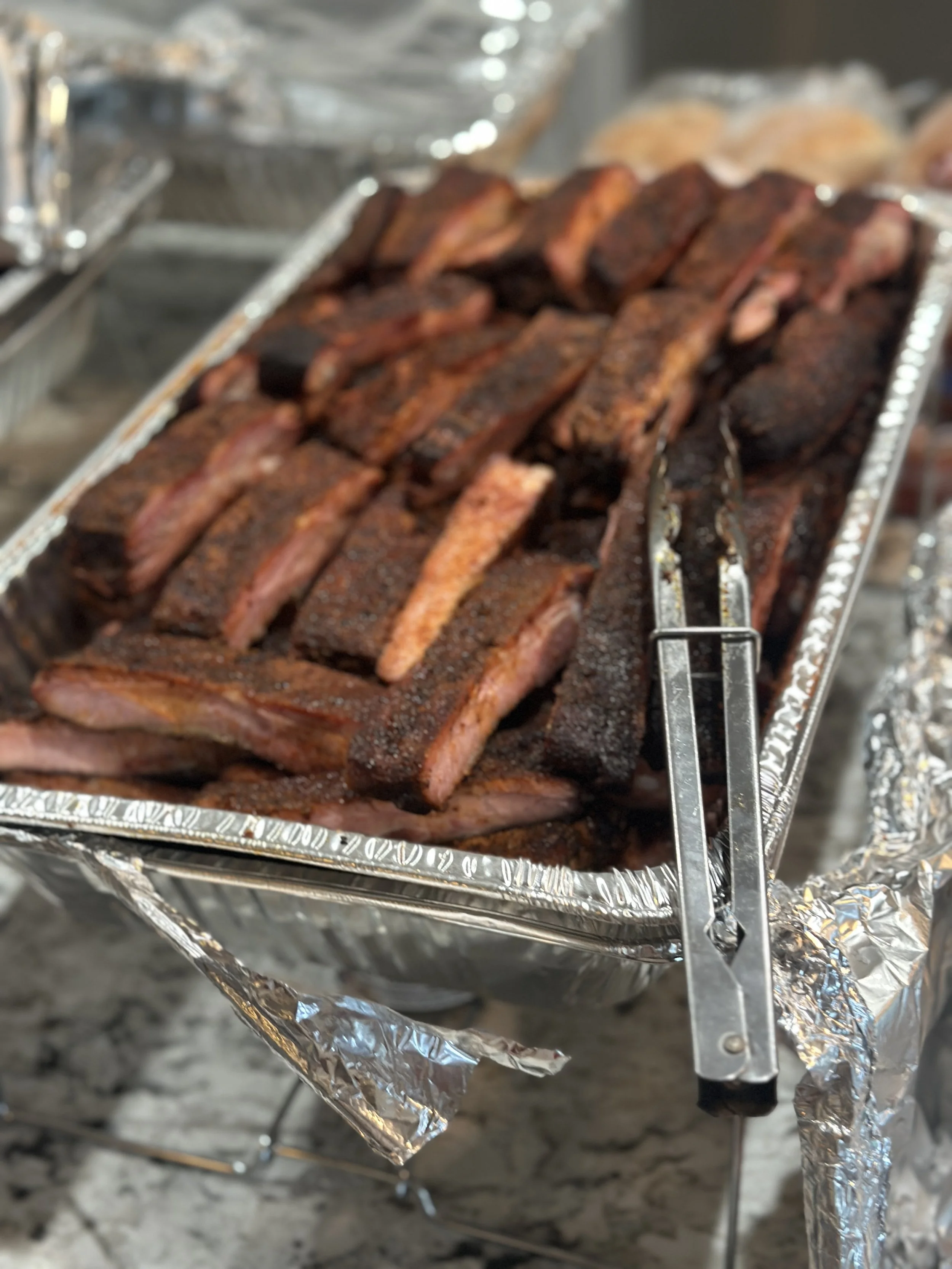 Close-up of ribs on a grill wrapped in aluminum foil, with a grill thermometer inserted in one of the ribs