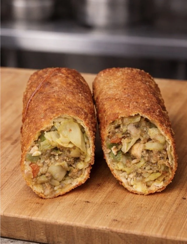 Cross-section of two crispy, golden-fried vegetable and meat croquettes on a wooden cutting board, showing a filling of chopped vegetables and ground meat.