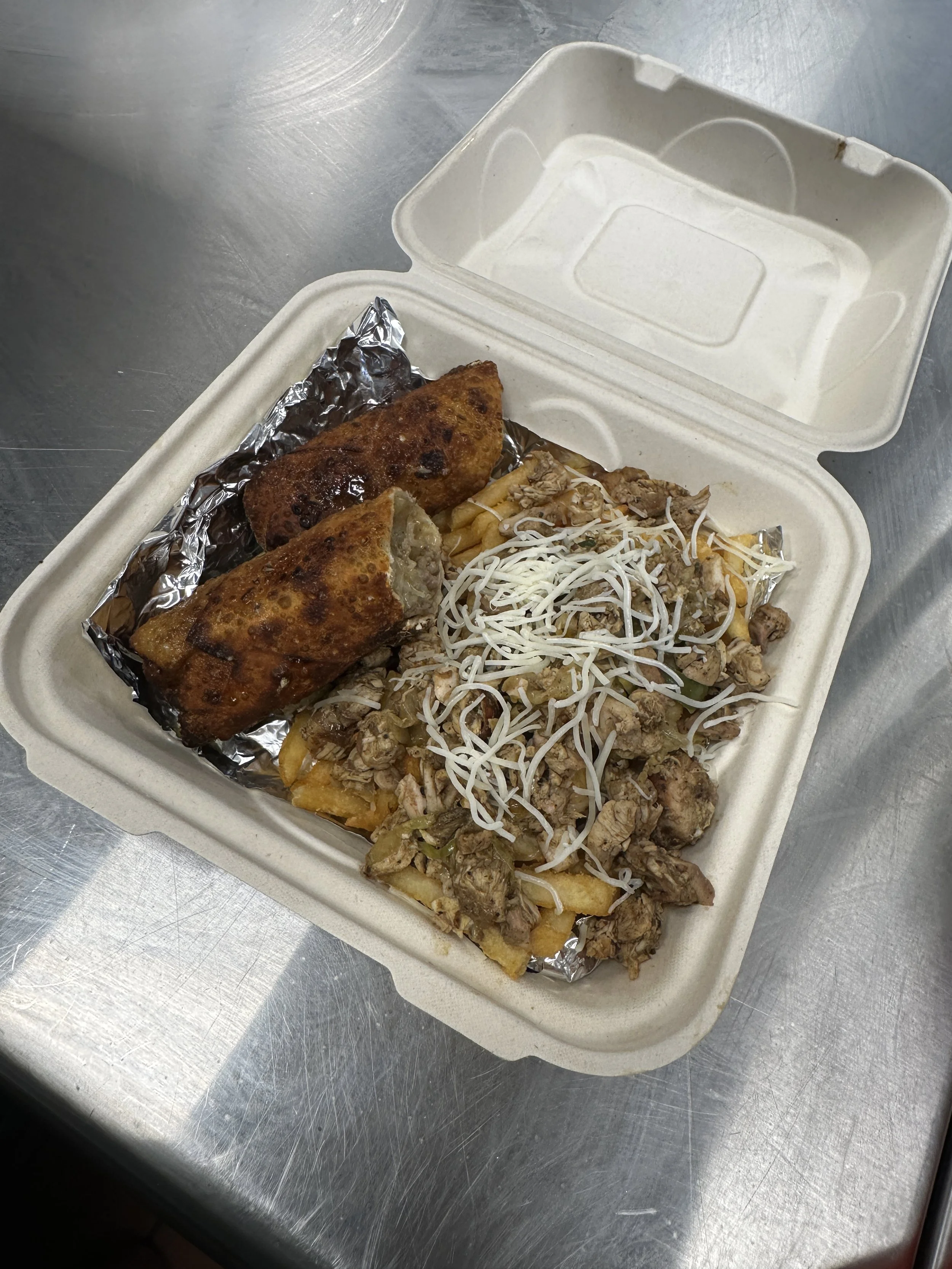 Takeout container with two fried egg rolls and a serving of chopped meat topped with shredded cheese and shredded cabbage on a metal surface.