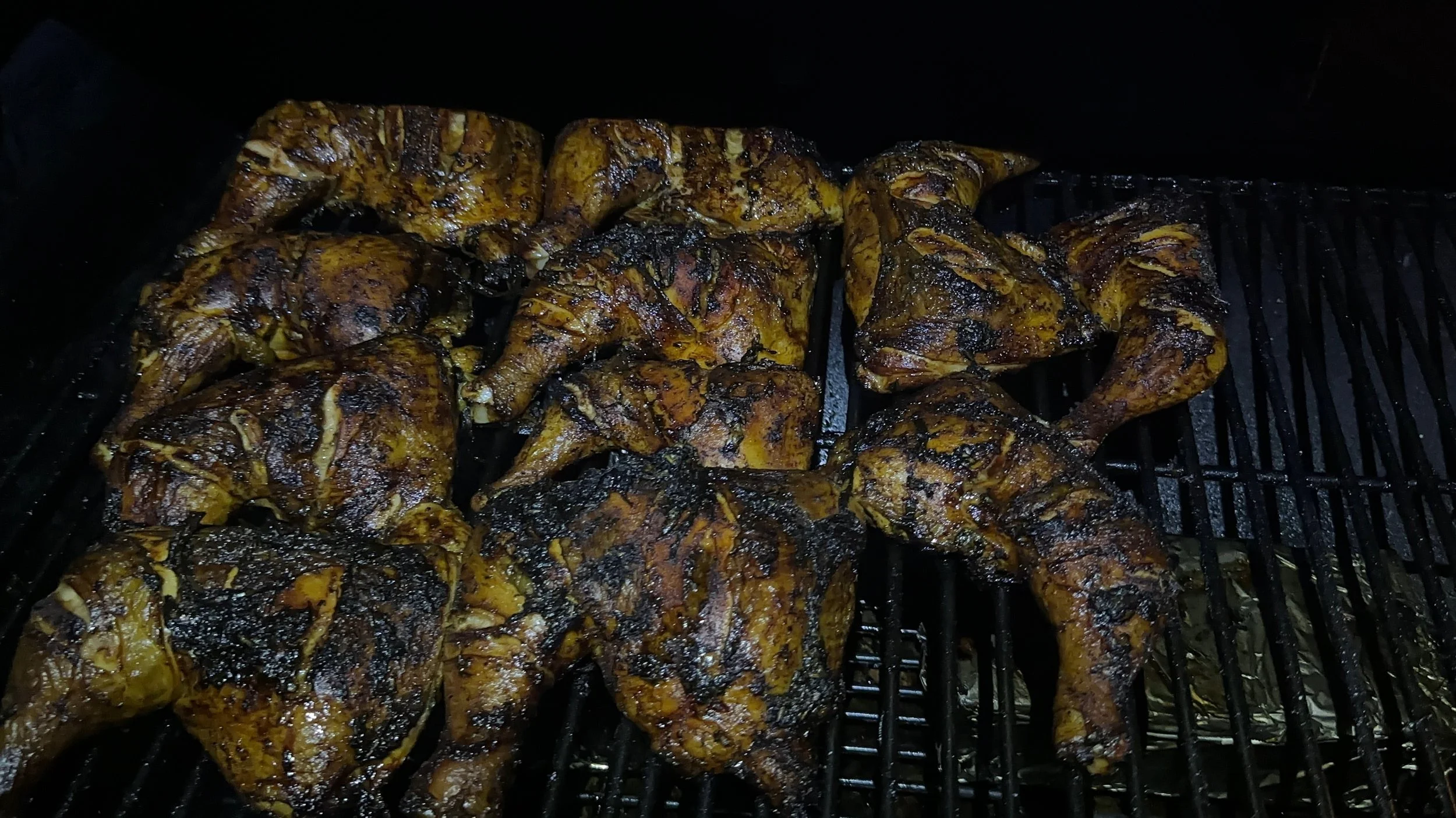 Cooked jerk chicken drumsticks with charred, crispy skin on a grill inside an oven.