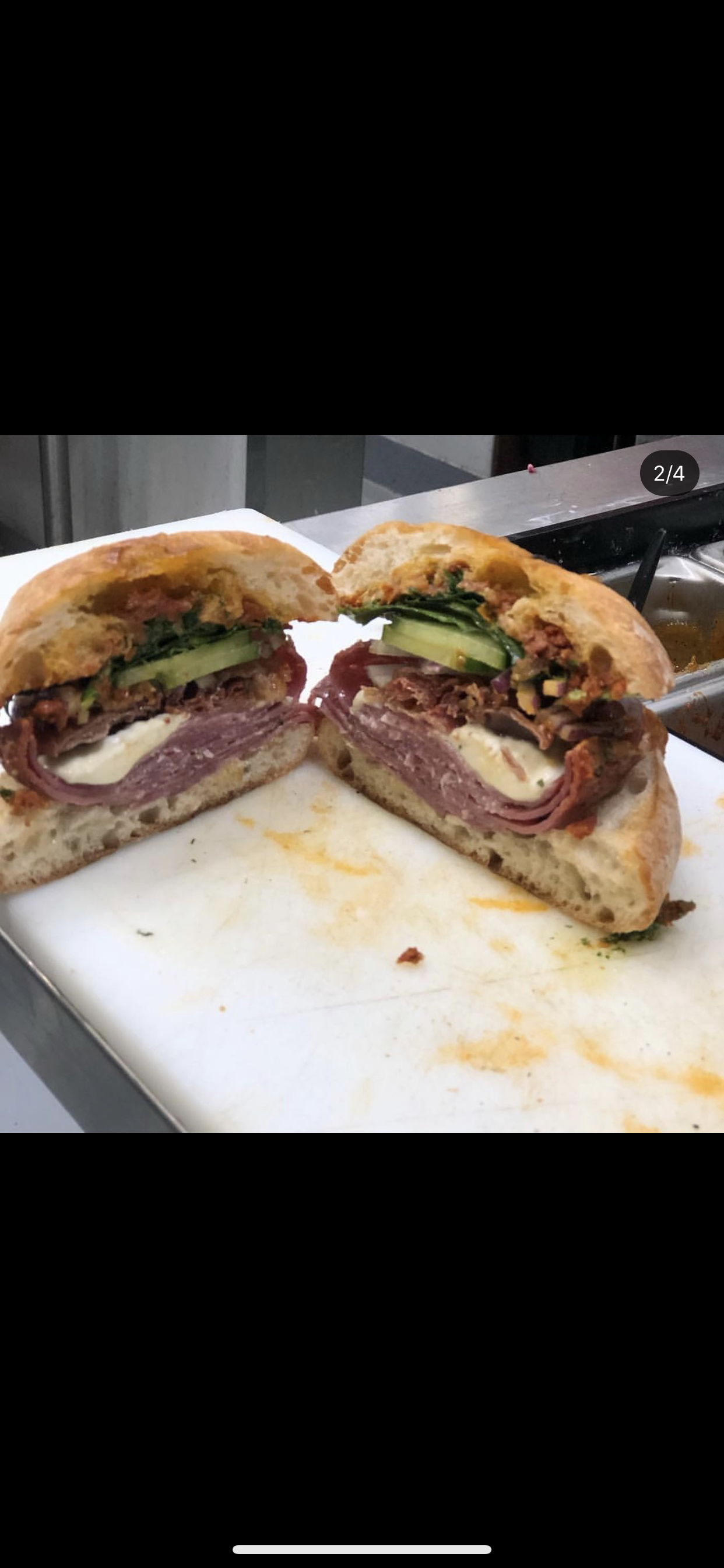 Cross-section of a large sandwich with roast beef, cheese, cucumber, and lettuce inside a toasted bun on a white cutting board.