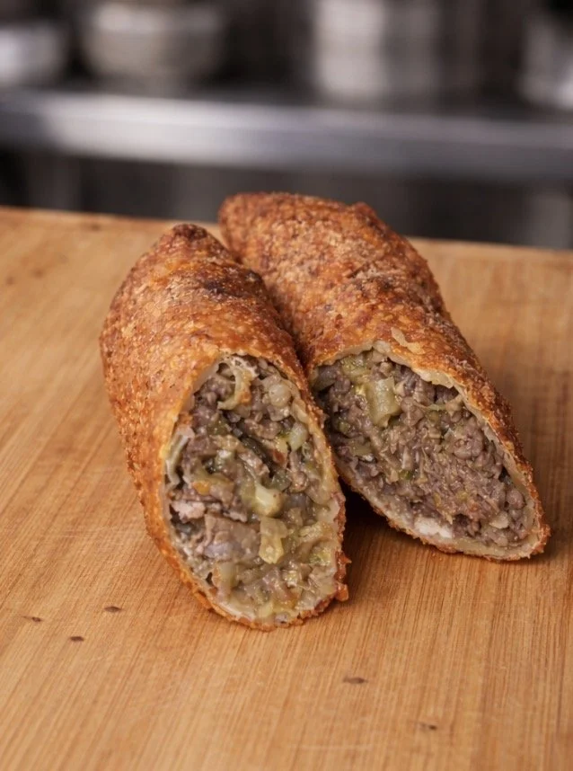 A cut-in-half beef and vegetable egg roll on a wooden cutting board.