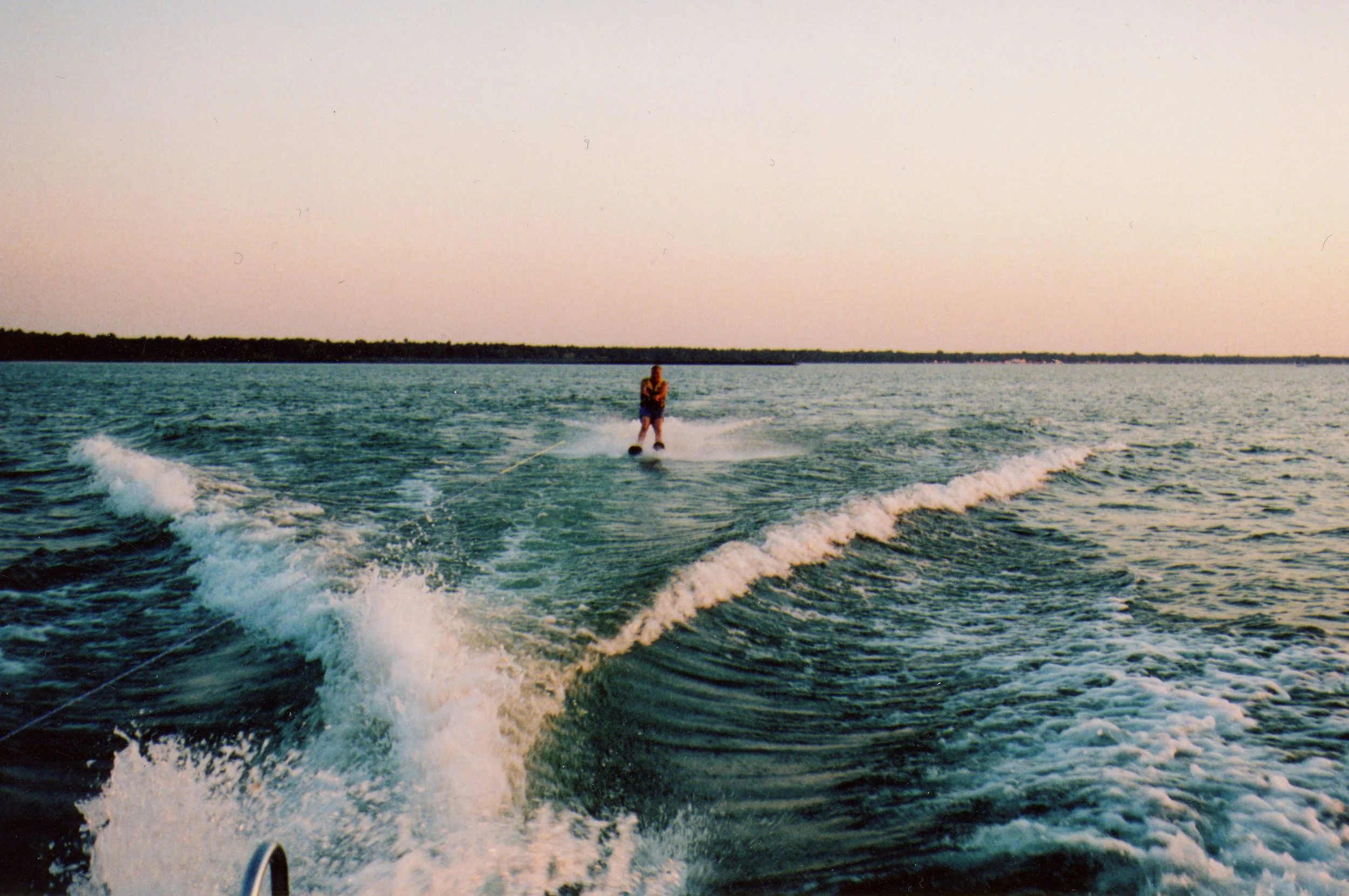 A person water skiing on a large body of water during sunset, with a distant shoreline in the background.