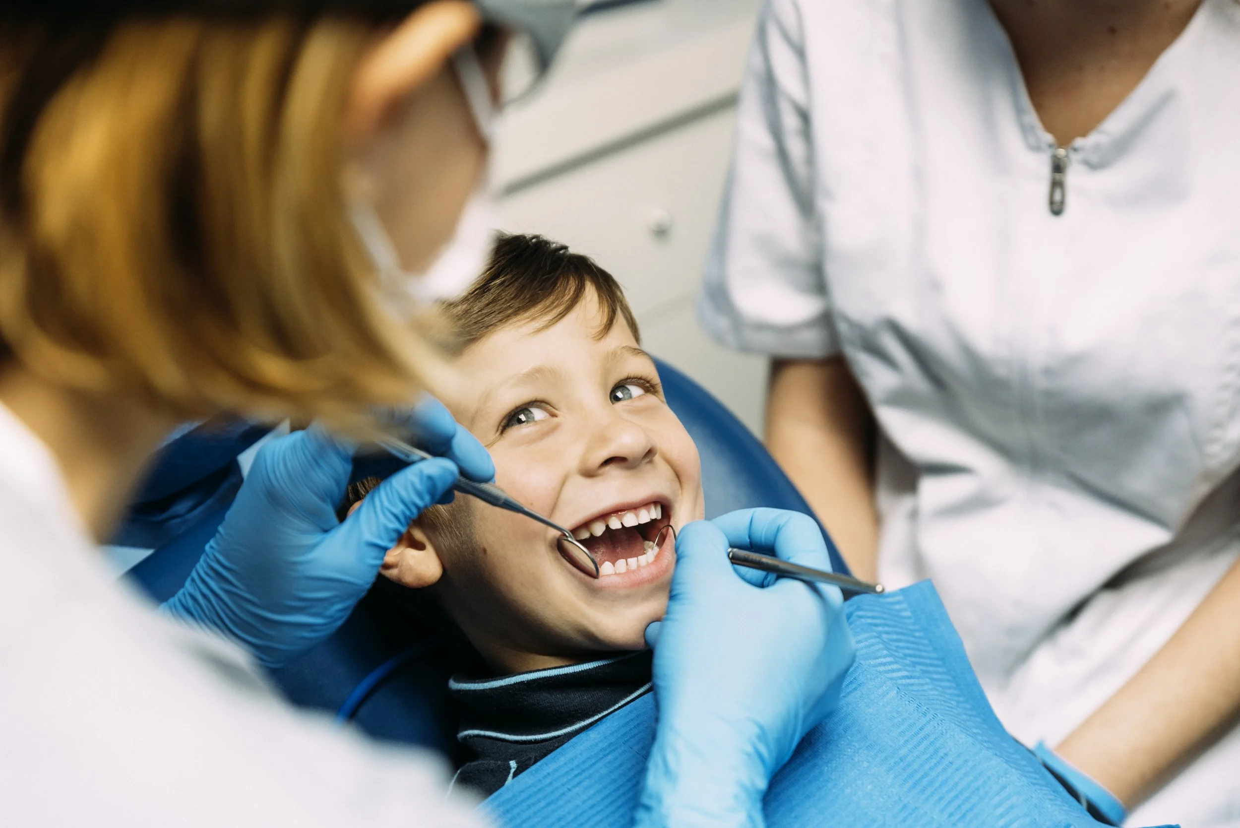 A young boy smiling happily during a dental check-up, with dental professionals examining his teeth.