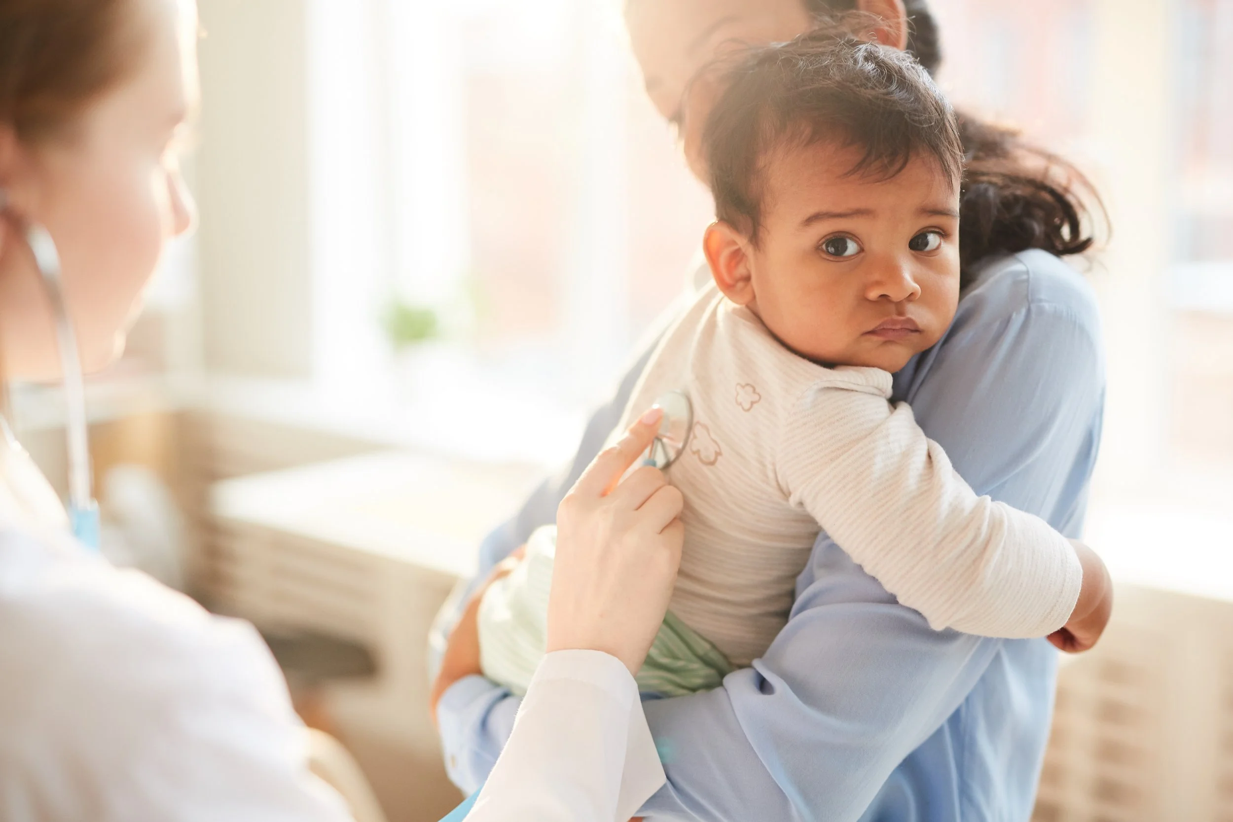 A healthcare professional examines a young child with a stethoscope in a medical setting.