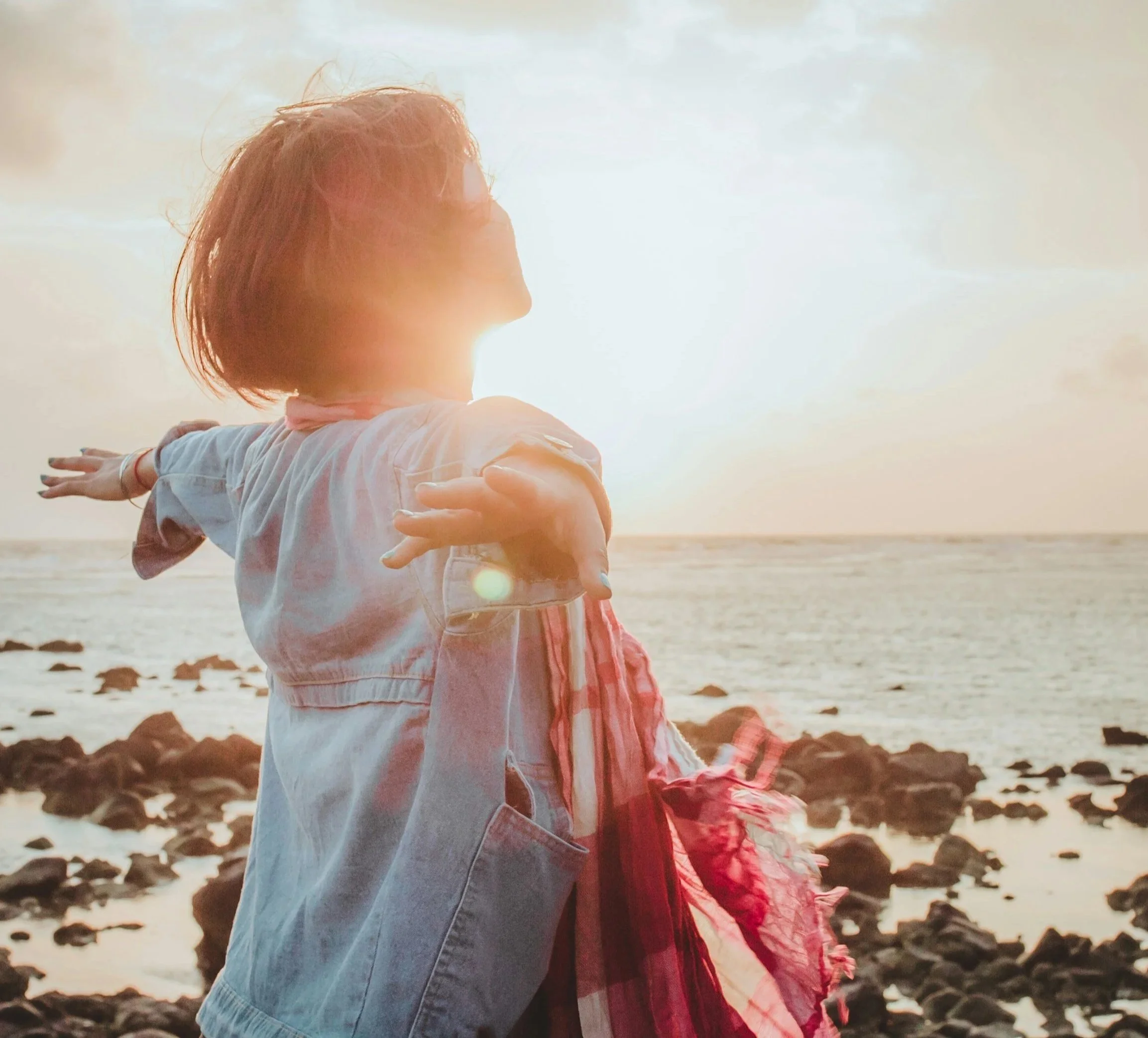 Woman standing peacefully along the shoreline with her arms outstretched, representing hope after grief and loss.