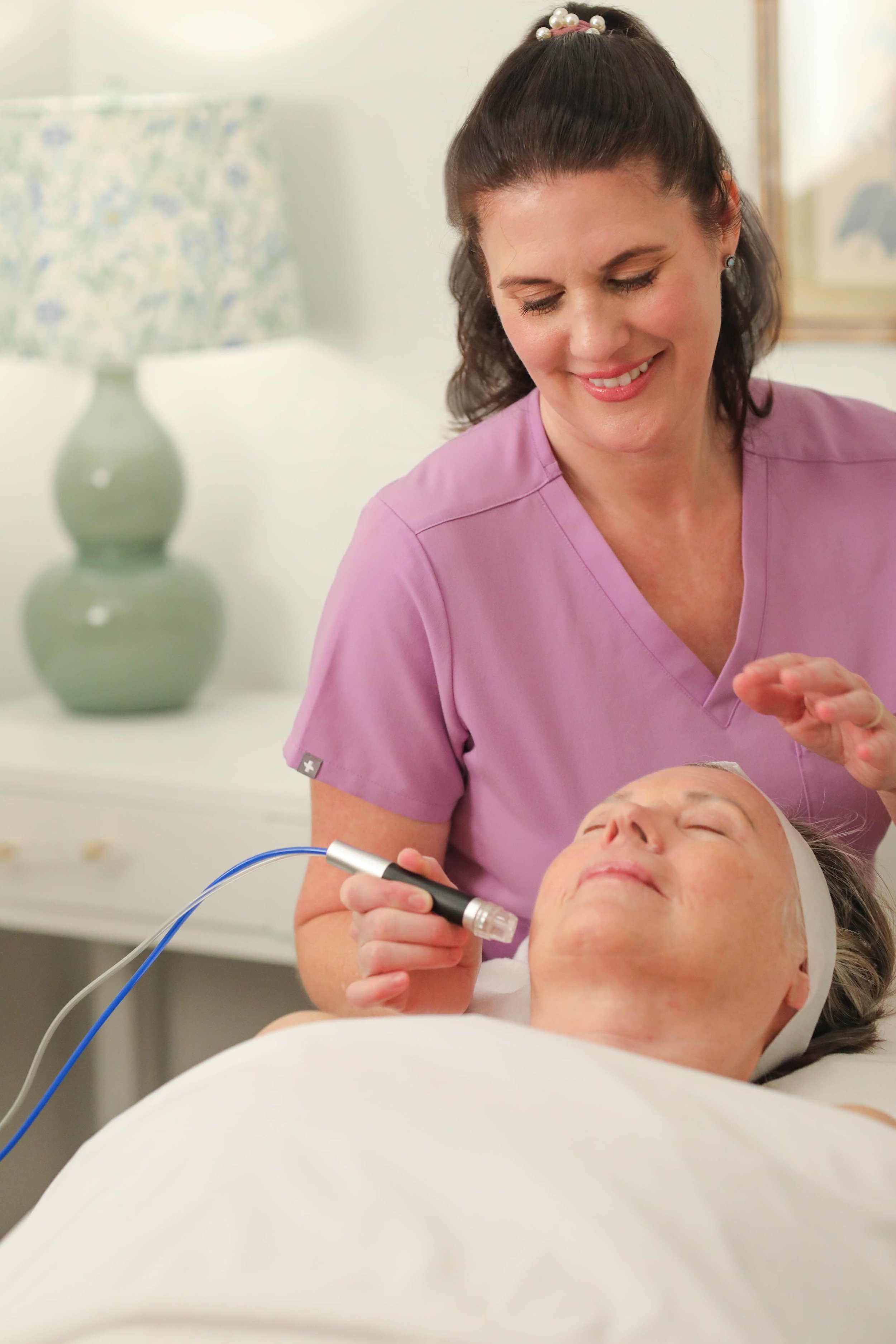 Paula smiling while performing a facial treatment in her light and fresh treatment room in Baton Rouge, LA.